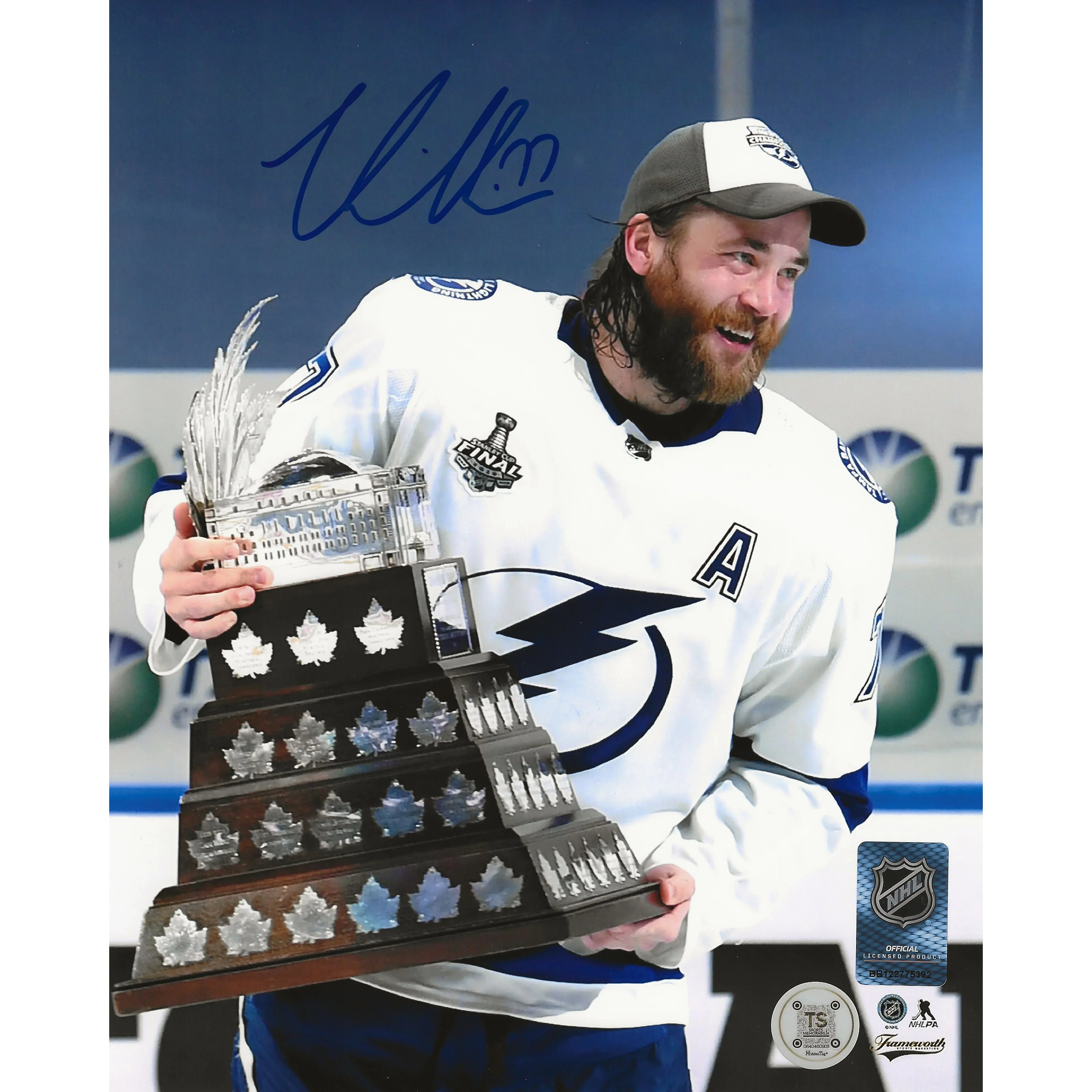 Hockey player in Tampa Bay Lightning jersey holding large NHL trophy, smiling on ice rink.