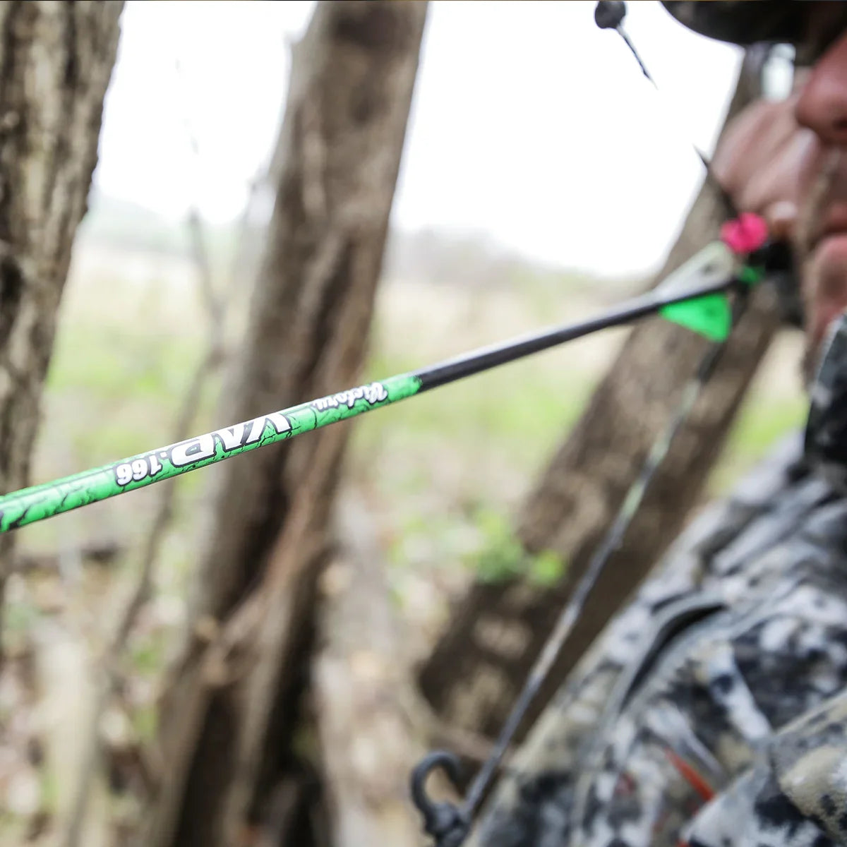 Close-up of hunter drawing camo VAP arrow with bow in wooded outdoor setting