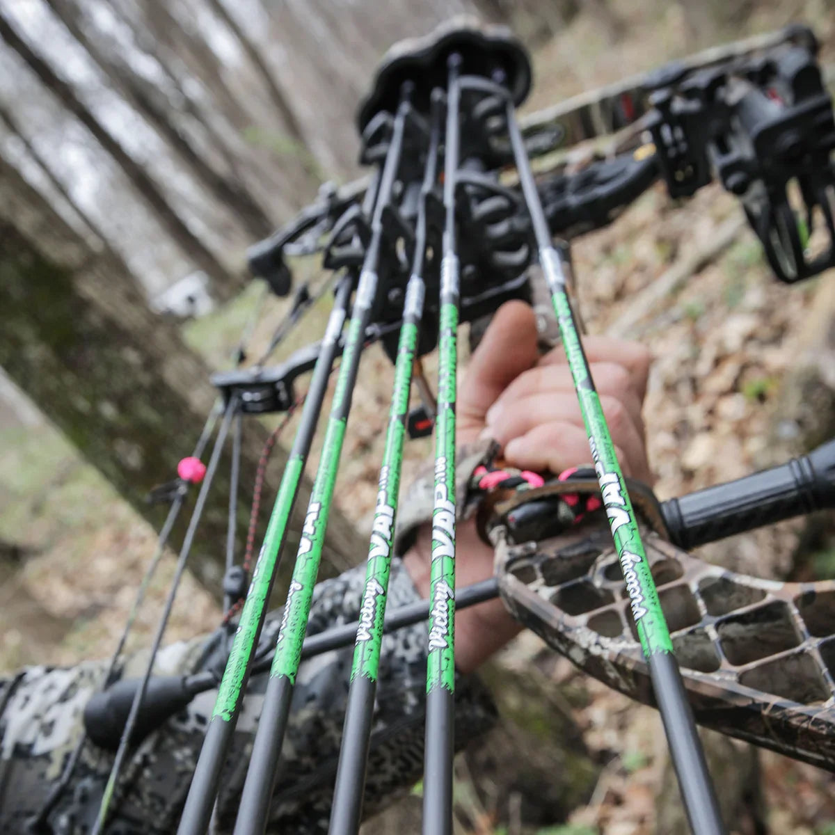 Hunter holding compound bow with green VAP Victory arrows in a forest setting