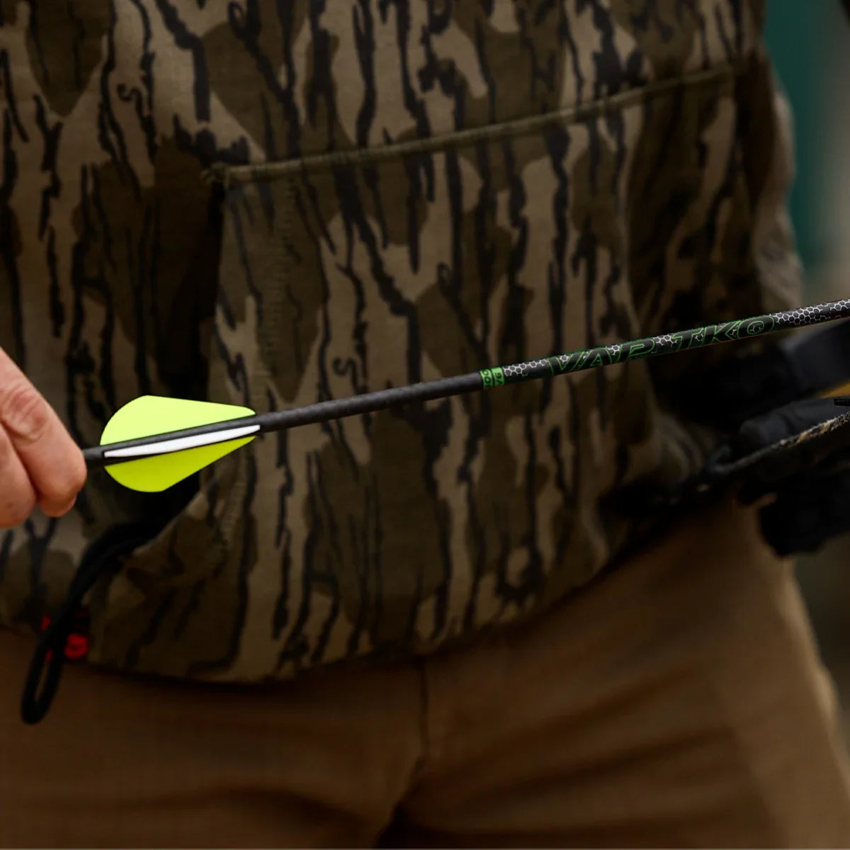 Person wearing camo jacket holding a VAP TKO carbon arrow with yellow vanes