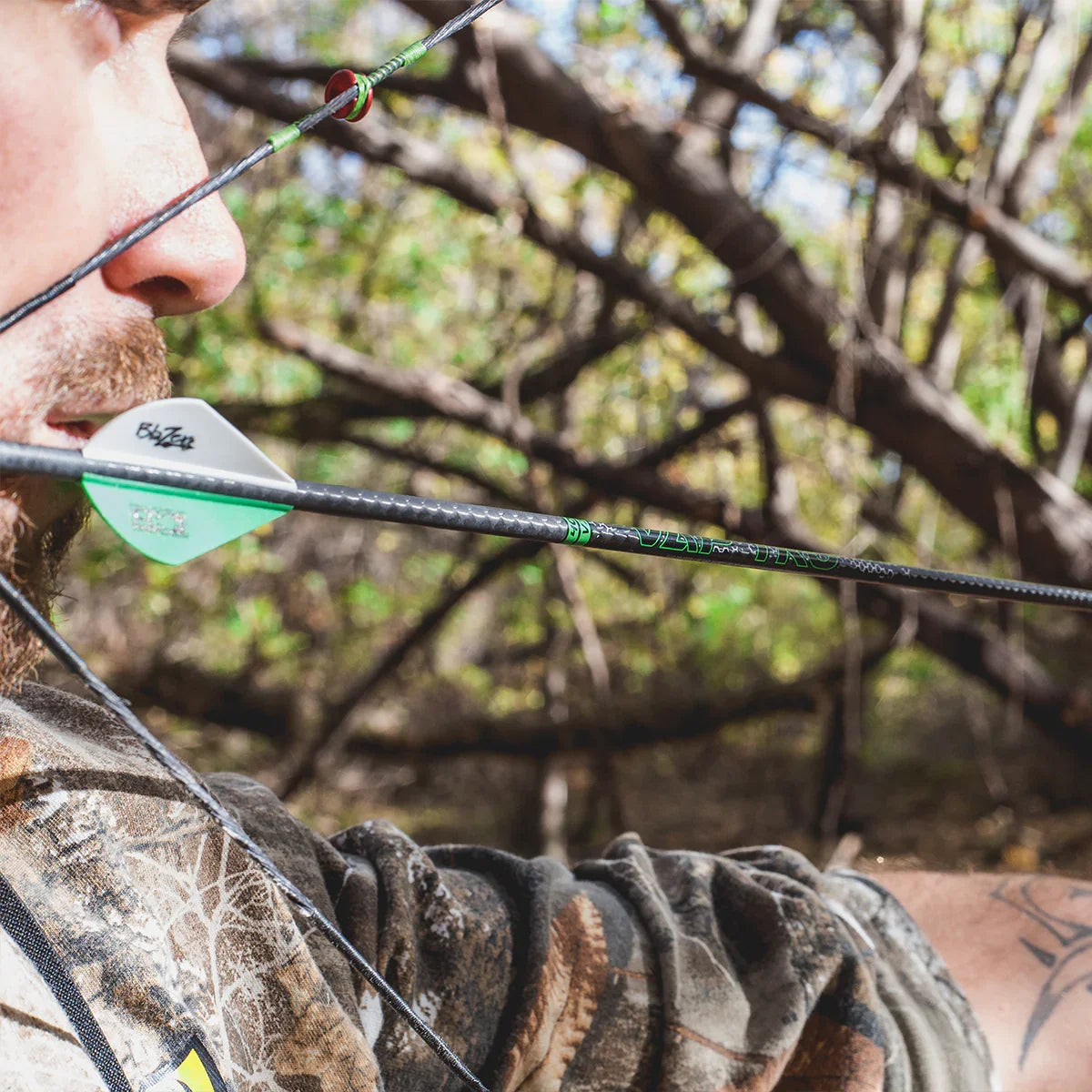 Close-up of archer aiming carbon arrow outdoors in camo gear, archery hunting scene
