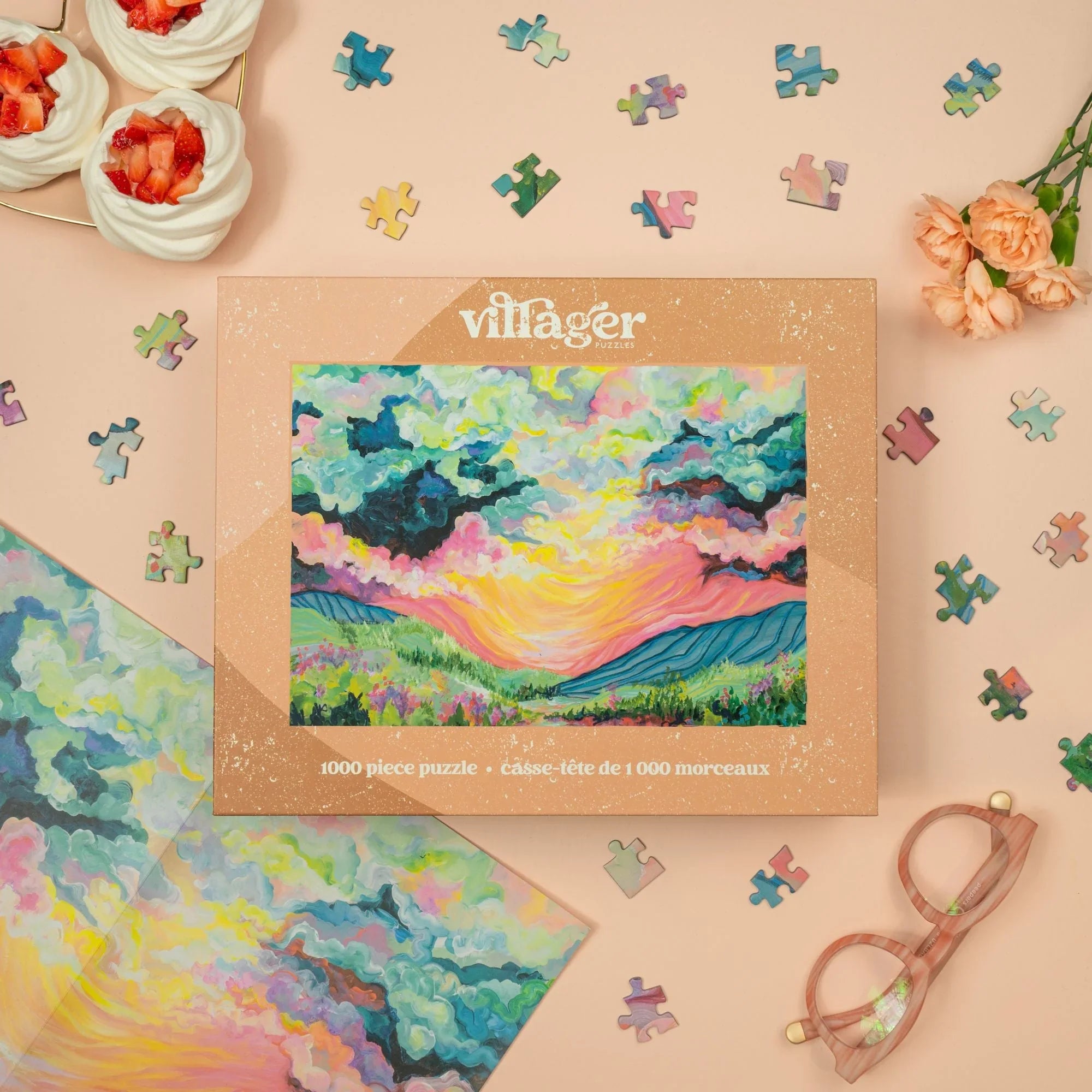 Villager Puzzles 1000 piece sunset landscape puzzle box on pink table with glasses, flowers, mini pavlovas, and colorful puzzle pieces.
