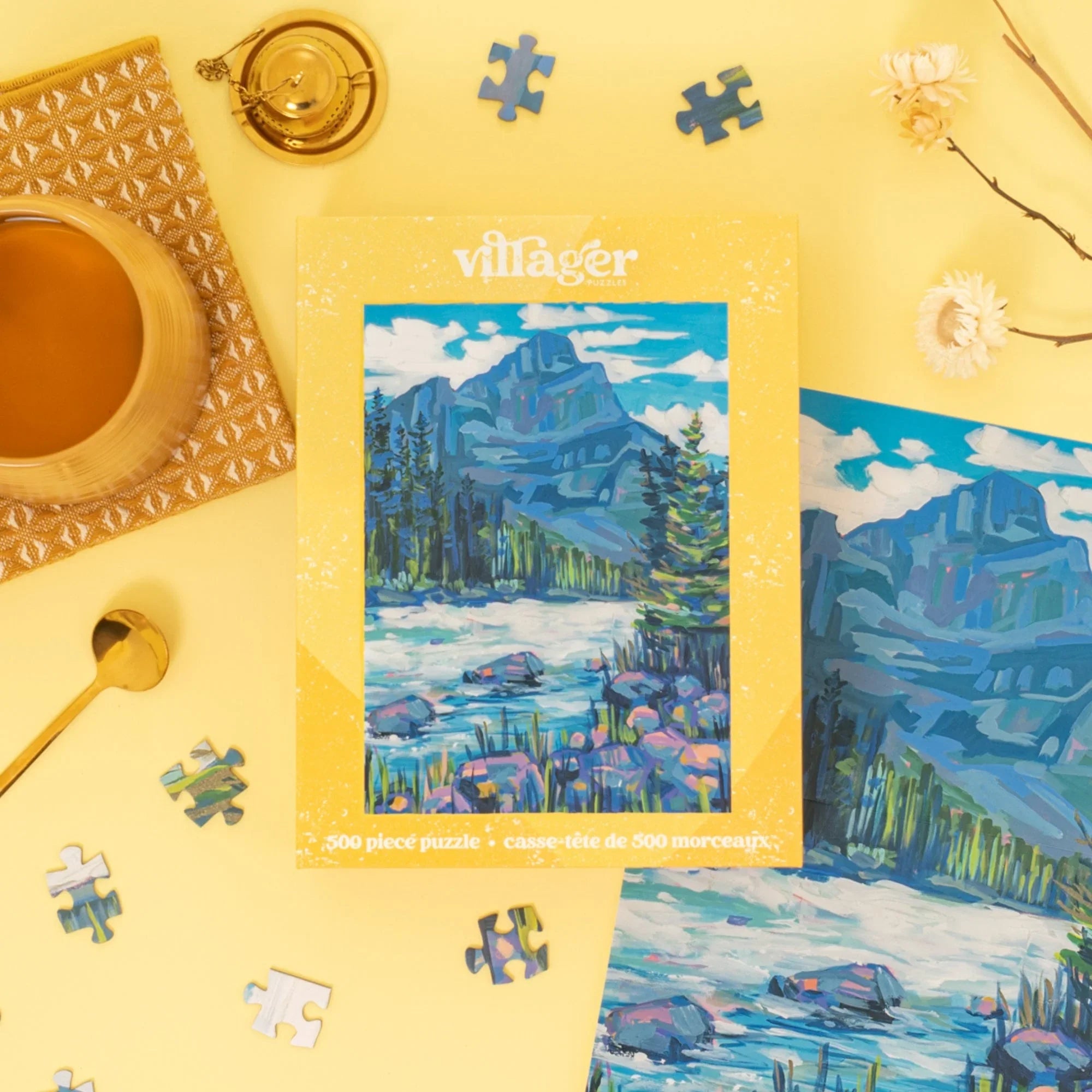 Kicking Horse mountain puzzle box with scattered pieces, tea, and flowers on yellow background