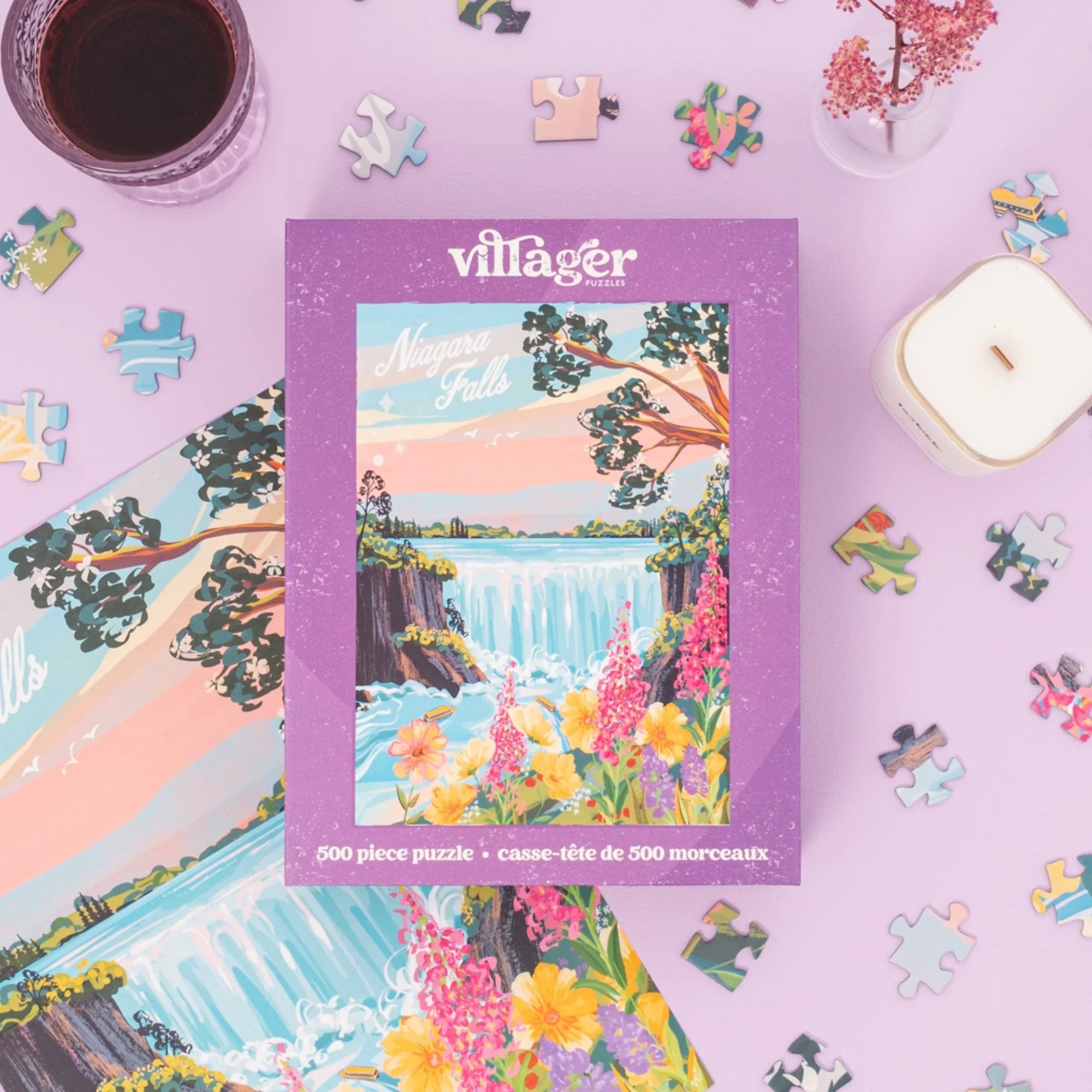 Niagara Falls puzzle box on pastel surface with puzzle pieces, candle, and glass of wine