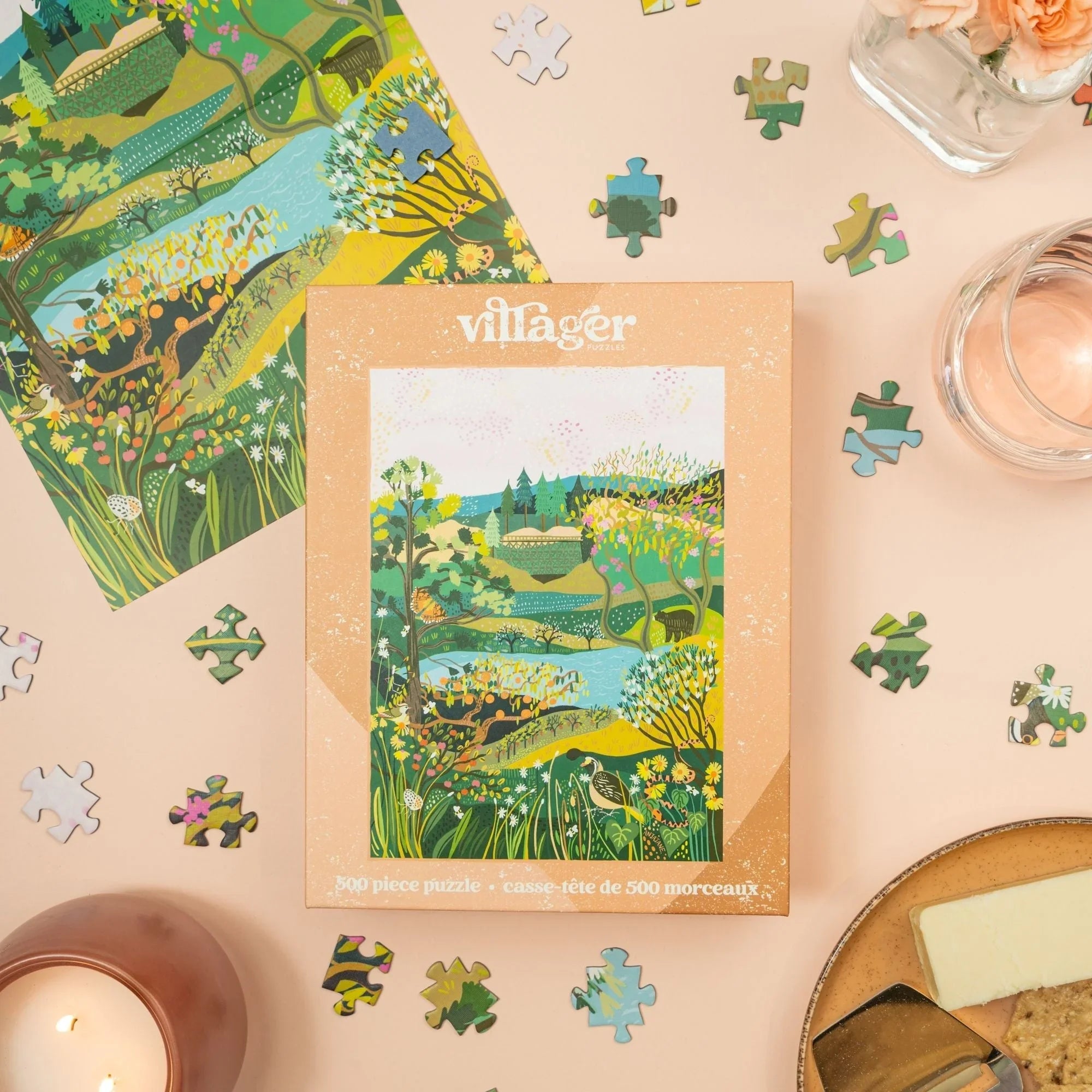 Villager 500 piece puzzle box with floral landscape, loose pieces, candle, and flowers on table
