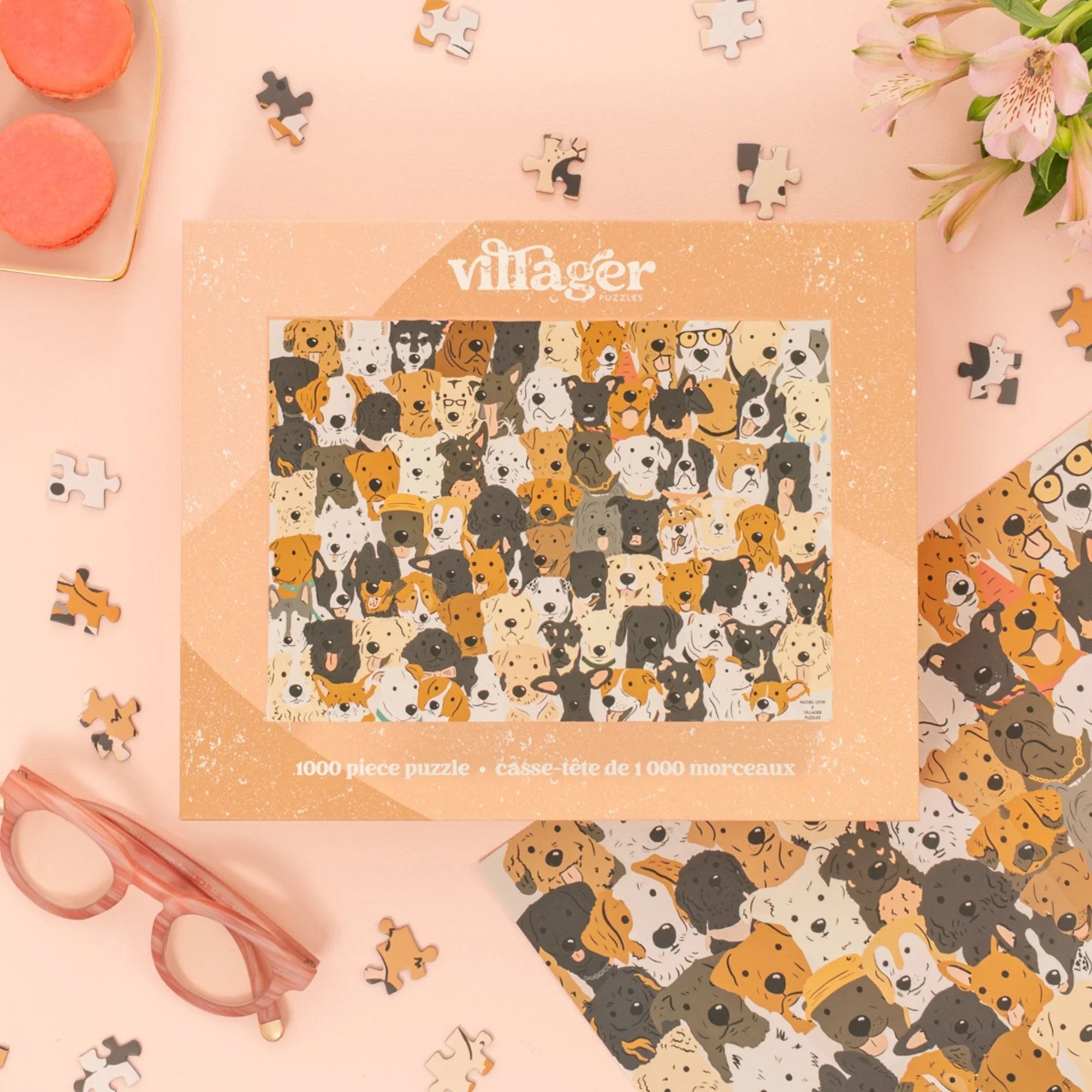 Villager rescue dogs puzzle box on pink table with flowers, macarons, glasses, and puzzle pieces.