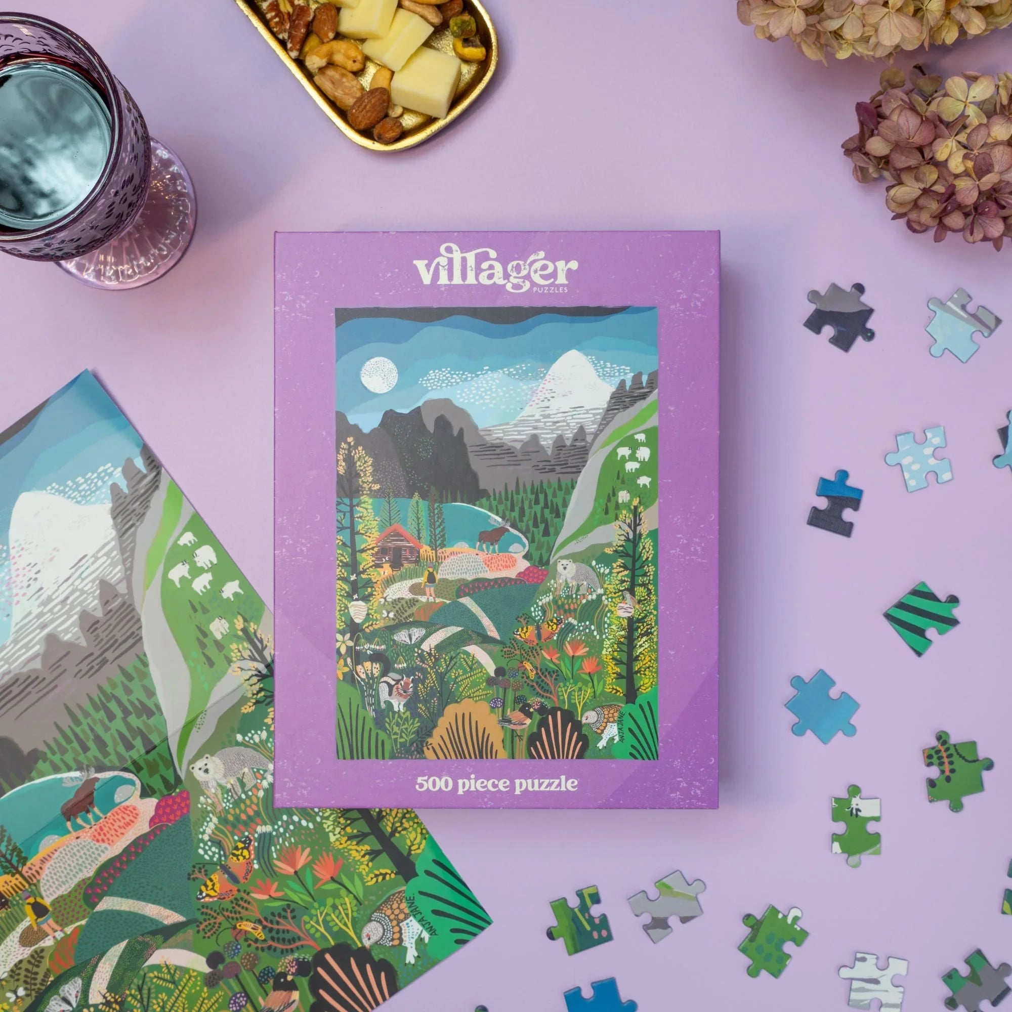 Villager Rockies Explorer 500 piece puzzle box on a lavender surface with scattered puzzle pieces, snacks, and flowers.