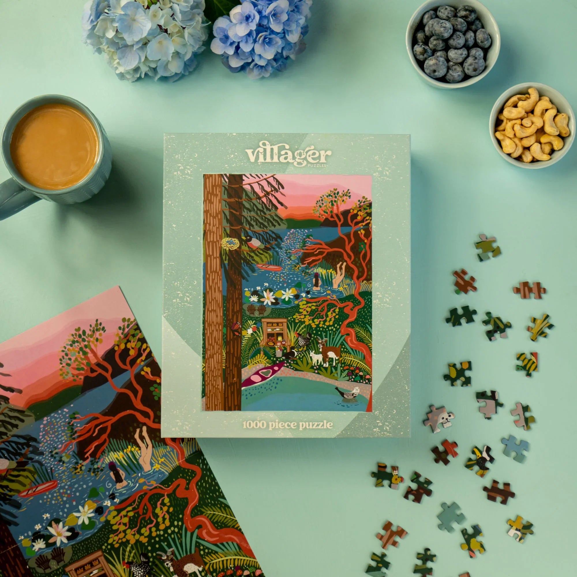 Villager 1000 piece puzzle box with colorful artwork, coffee, snacks, and flowers on blue table