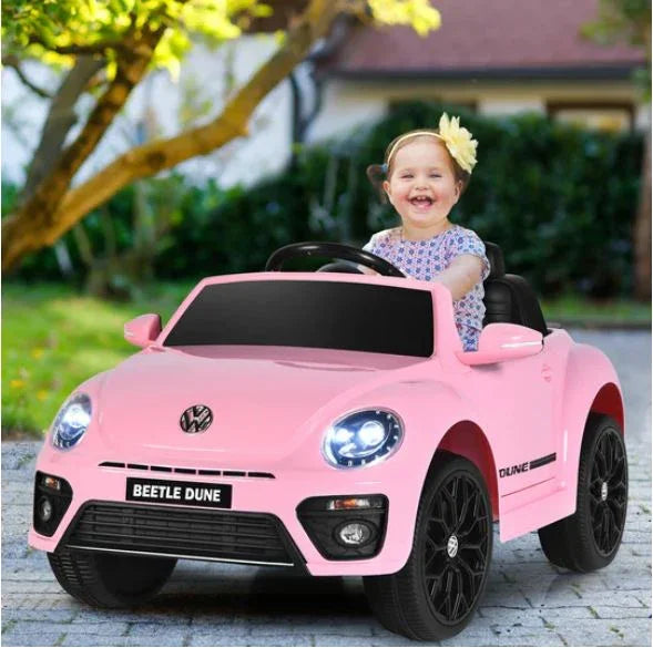 Smiling girl in pink Volkswagen Beetle Dune electric toy car outdoors