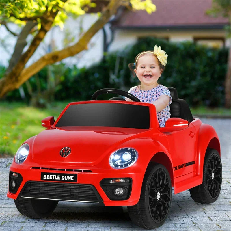 Smiling child driving red Volkswagen Beetle Dune electric ride-on car outdoors