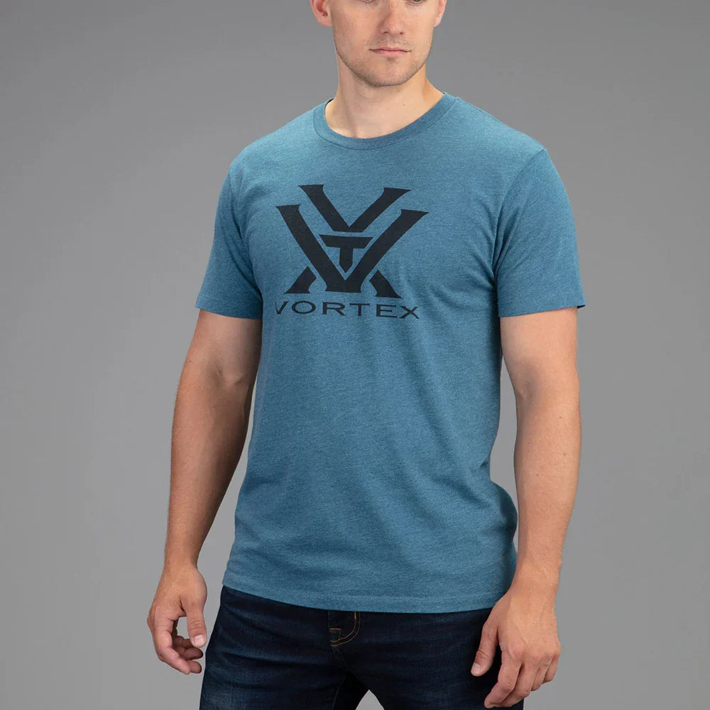 Man wearing blue Vortex T-shirt with large black logo, standing against a gray background