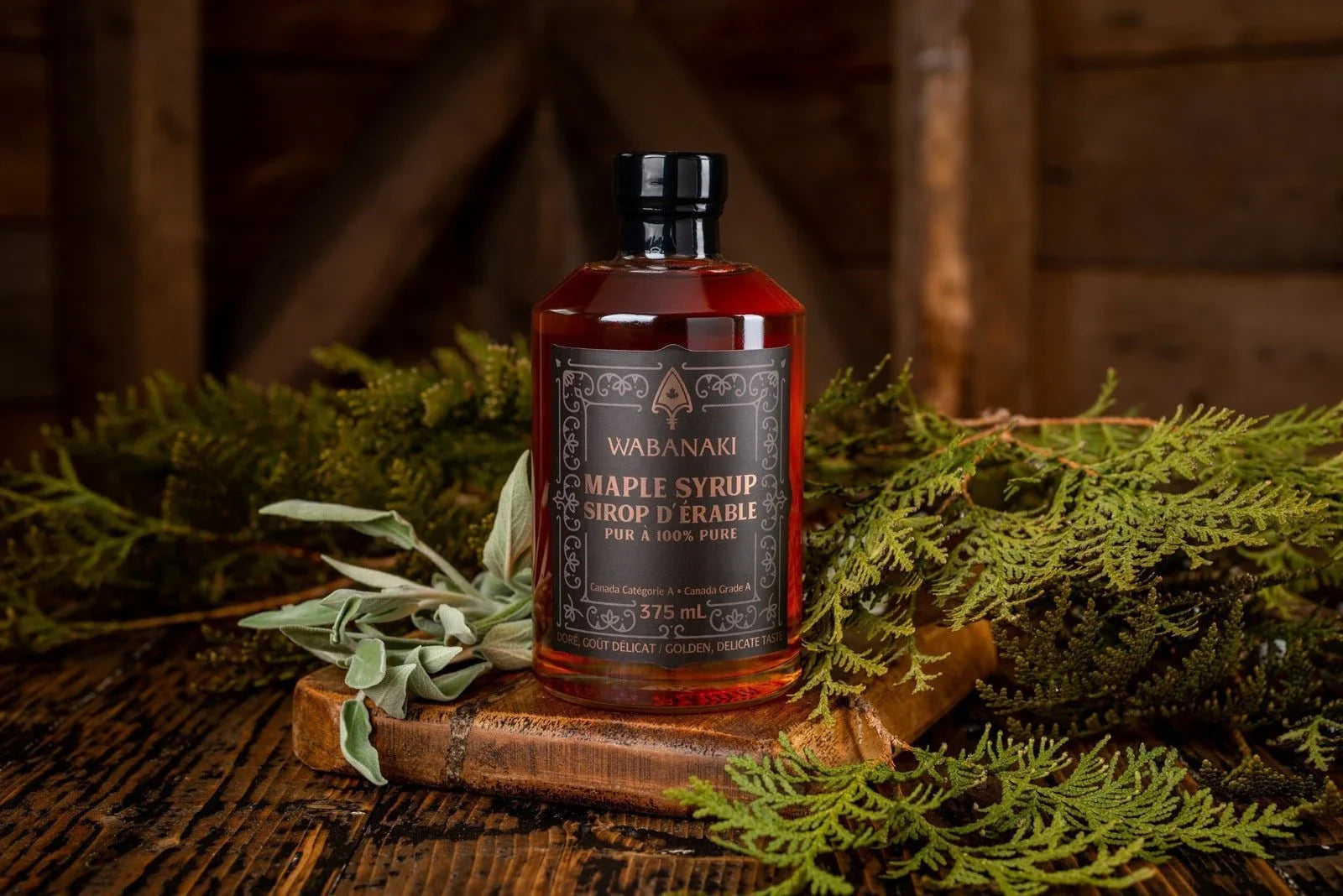 Wabanaki maple syrup bottle on rustic wood with green foliage, artisanal Canadian syrup