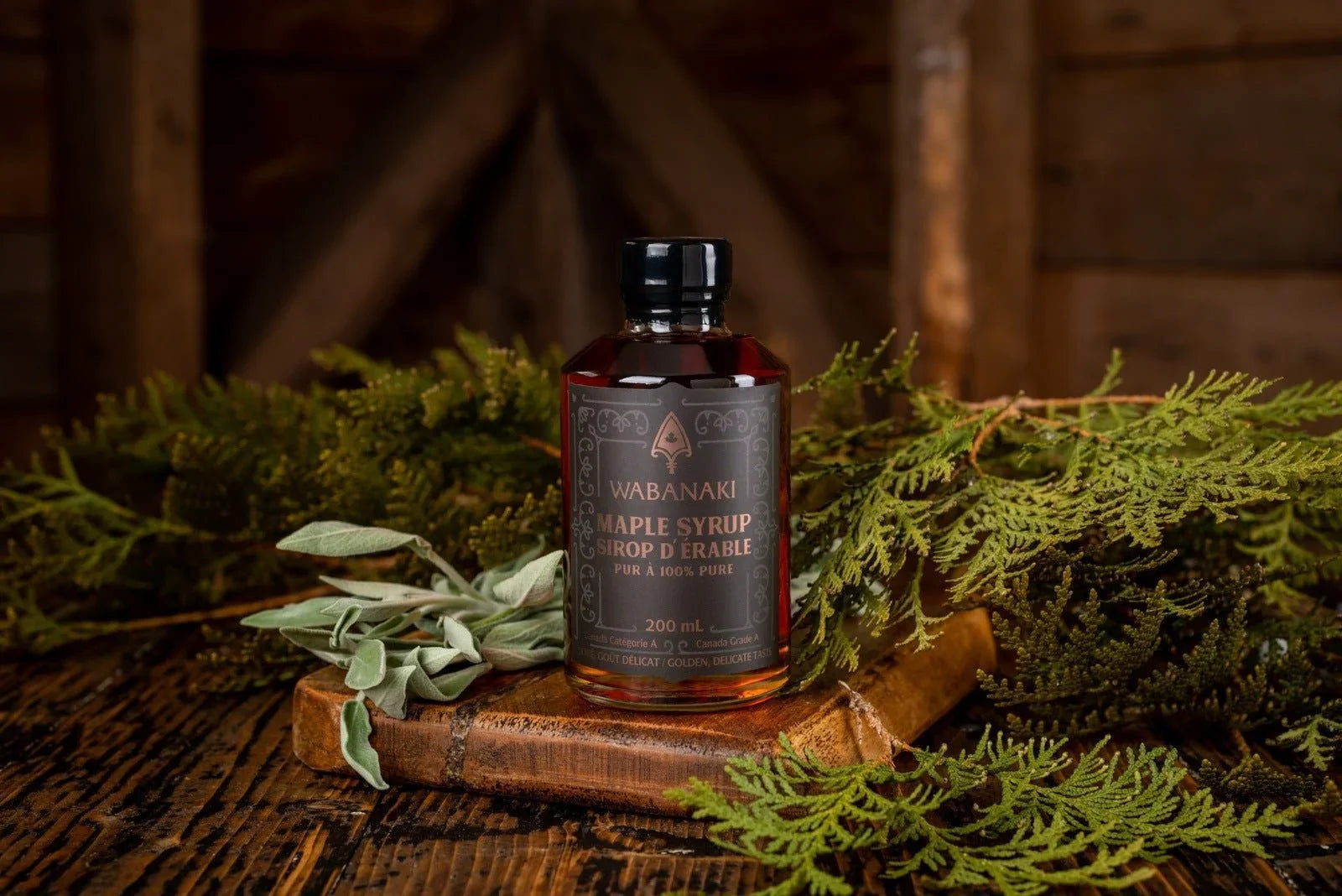 Wabanaki maple syrup bottle on rustic wood with green foliage and brown barn background