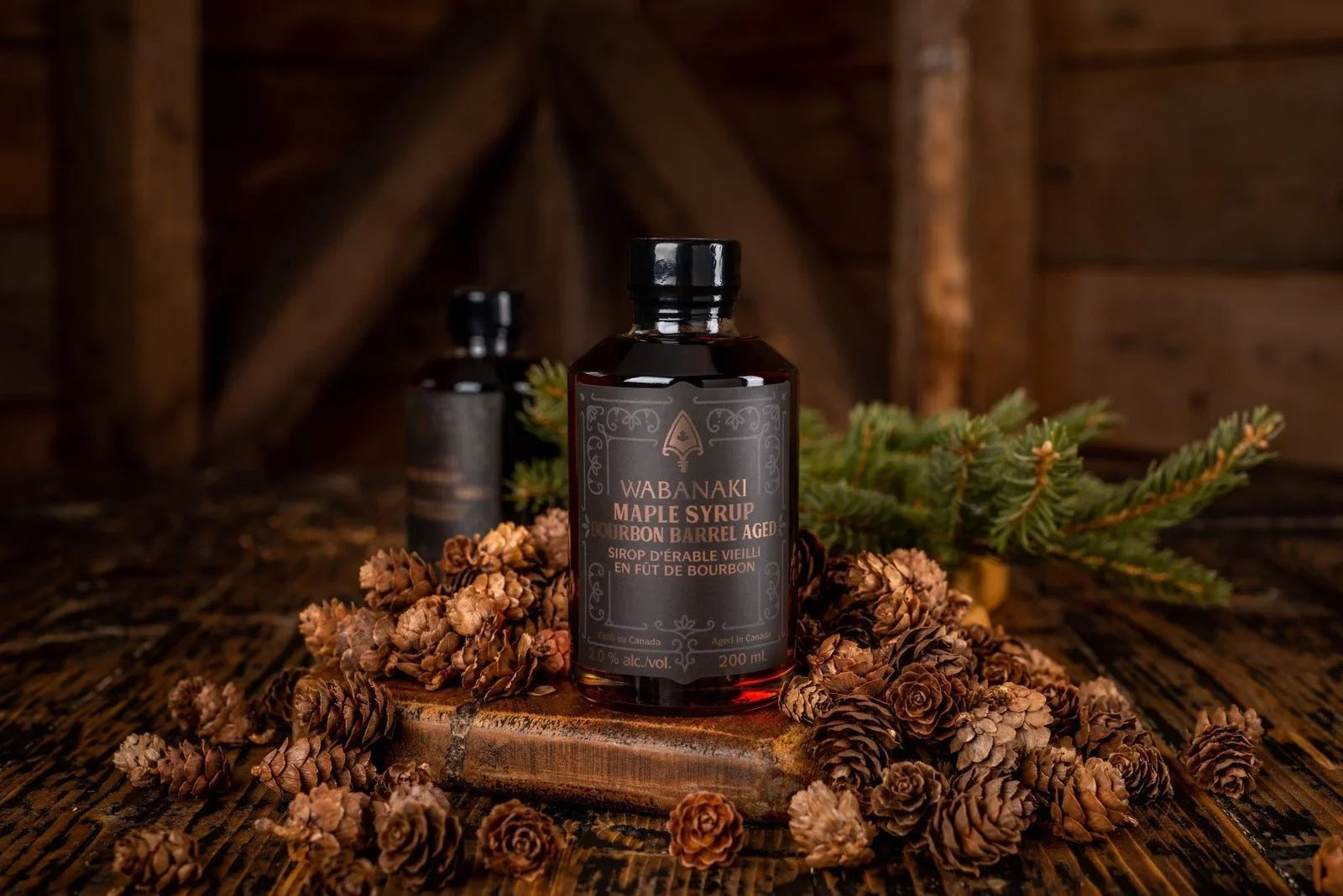 Wabanaki Bourbon Barrel Aged Maple Syrup bottle with pinecones on rustic wood table