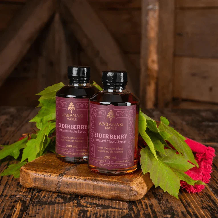 Wabanaki Maple elderberry infused maple syrup bottles with green leaves on wooden table