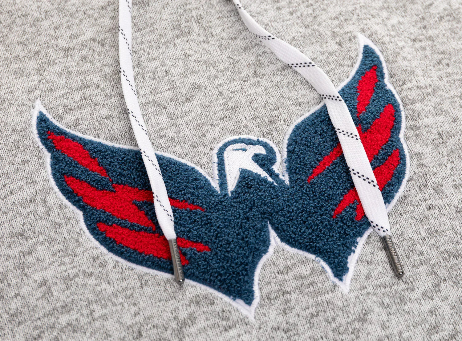 Close-up of grey hoodie with textured blue and red winged bird embroidered patch and white drawstrings