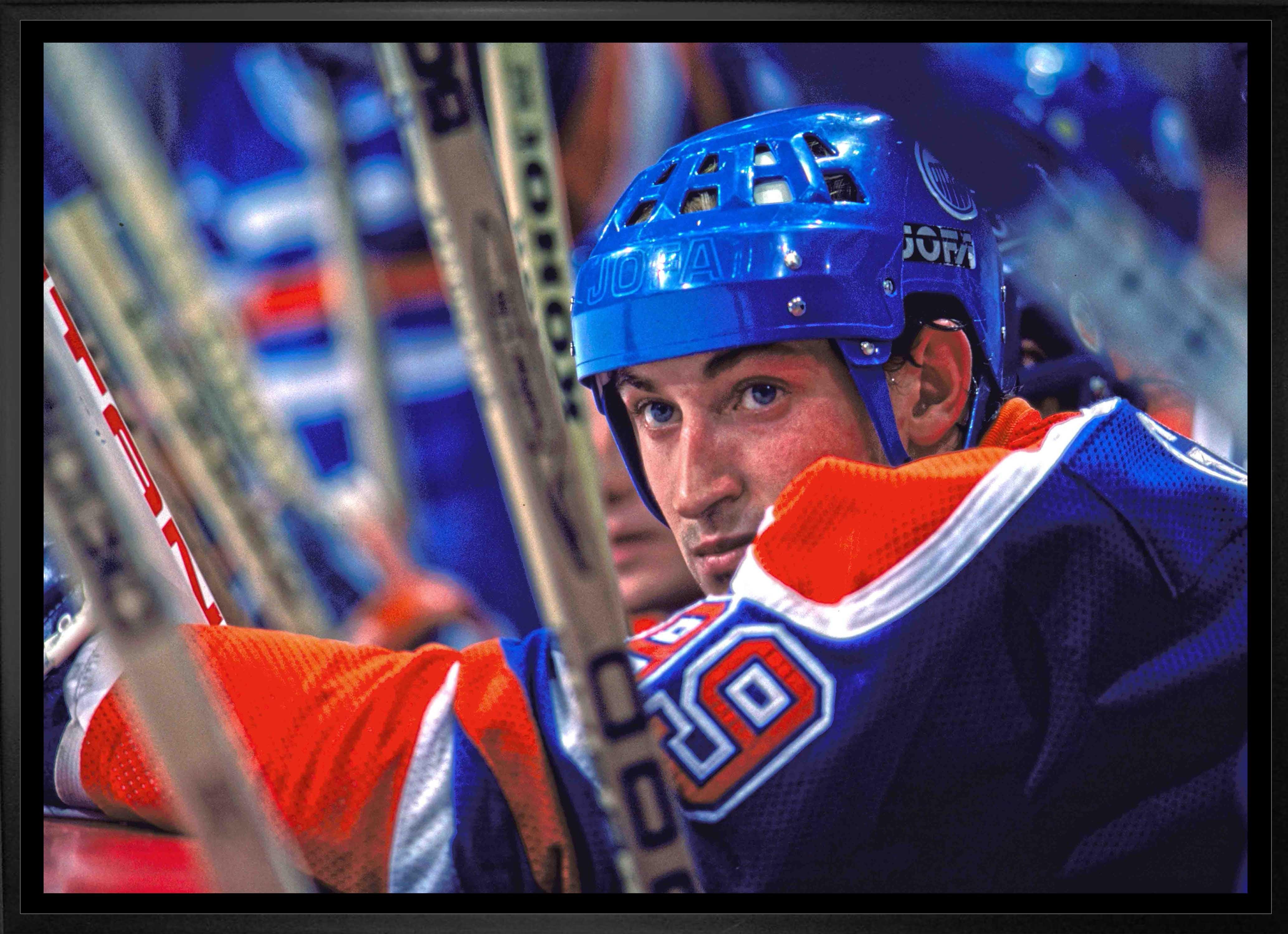Hockey player in blue helmet and jersey sitting on bench with hockey sticks, arena background