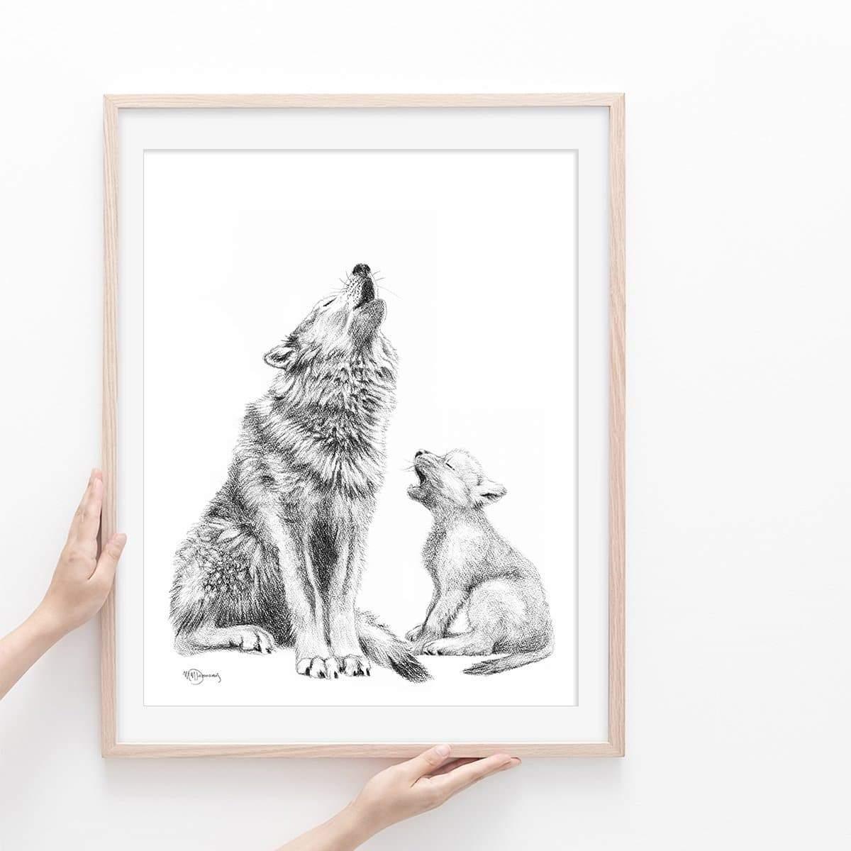 Framed black and white illustration of a howling wolf with cub, held by hands against white wall