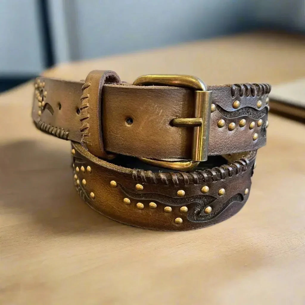 Women's full grain leather belt with geometric embossing, brass studs, and buckle on a table.