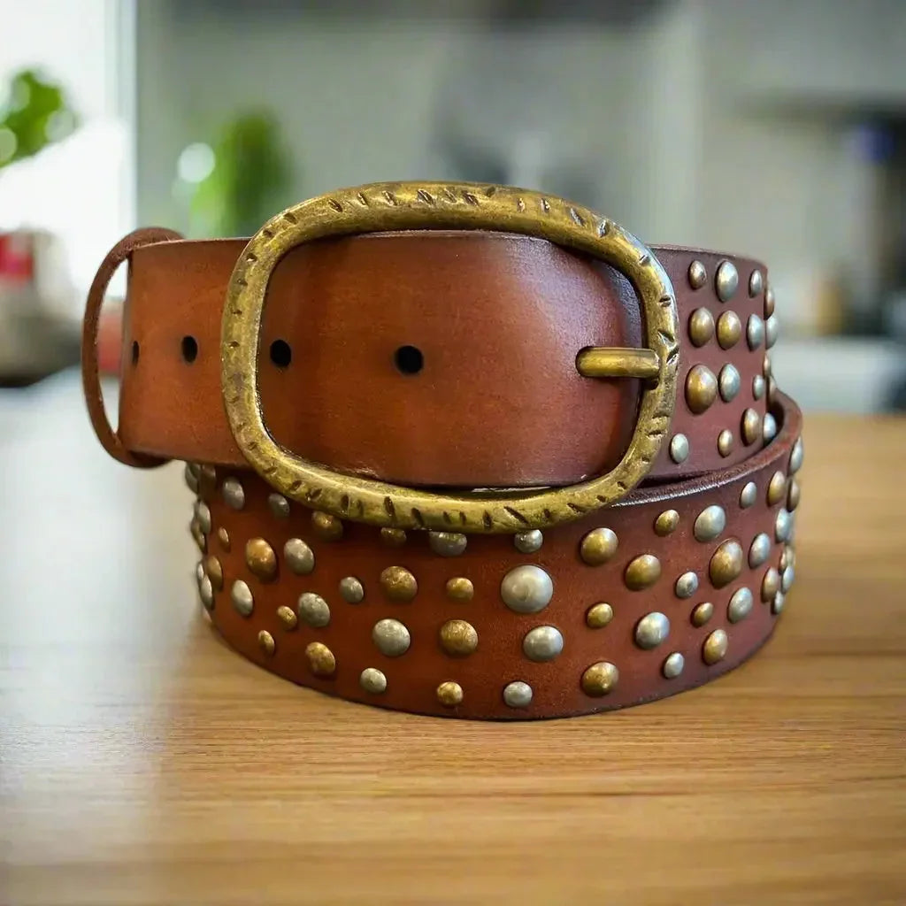 Women's full-grain leather belt with oval brass buckle and metal studs on wood surface