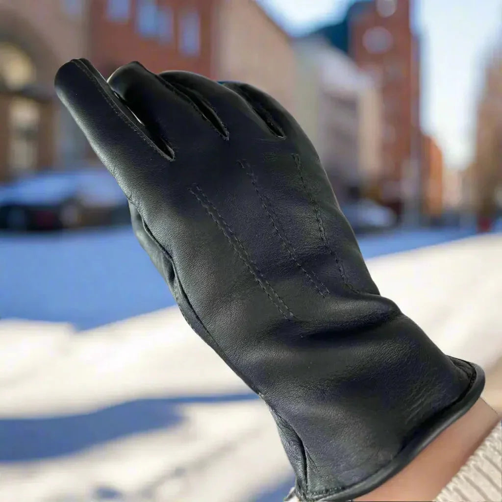 Black women's leather glove with fur lining outdoors in a snowy urban setting