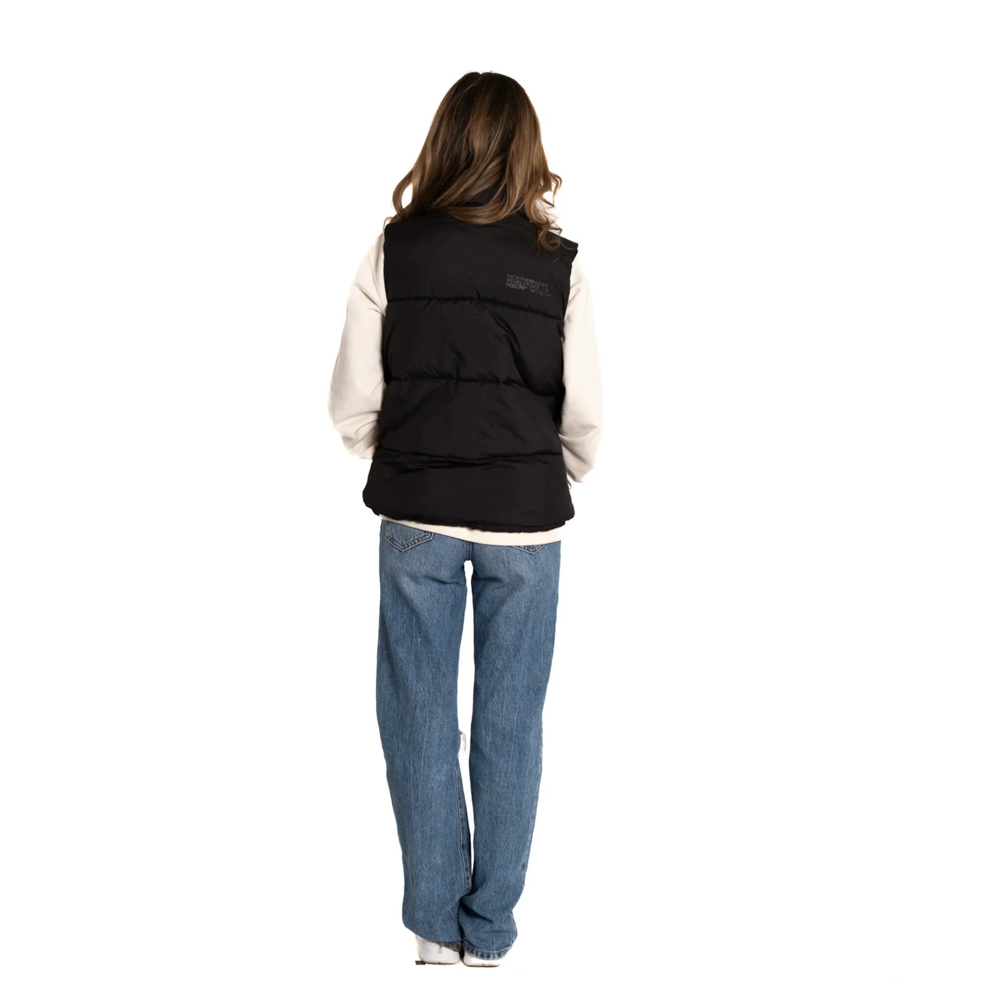 Woman in black puffer vest and jeans standing with back facing camera, white background