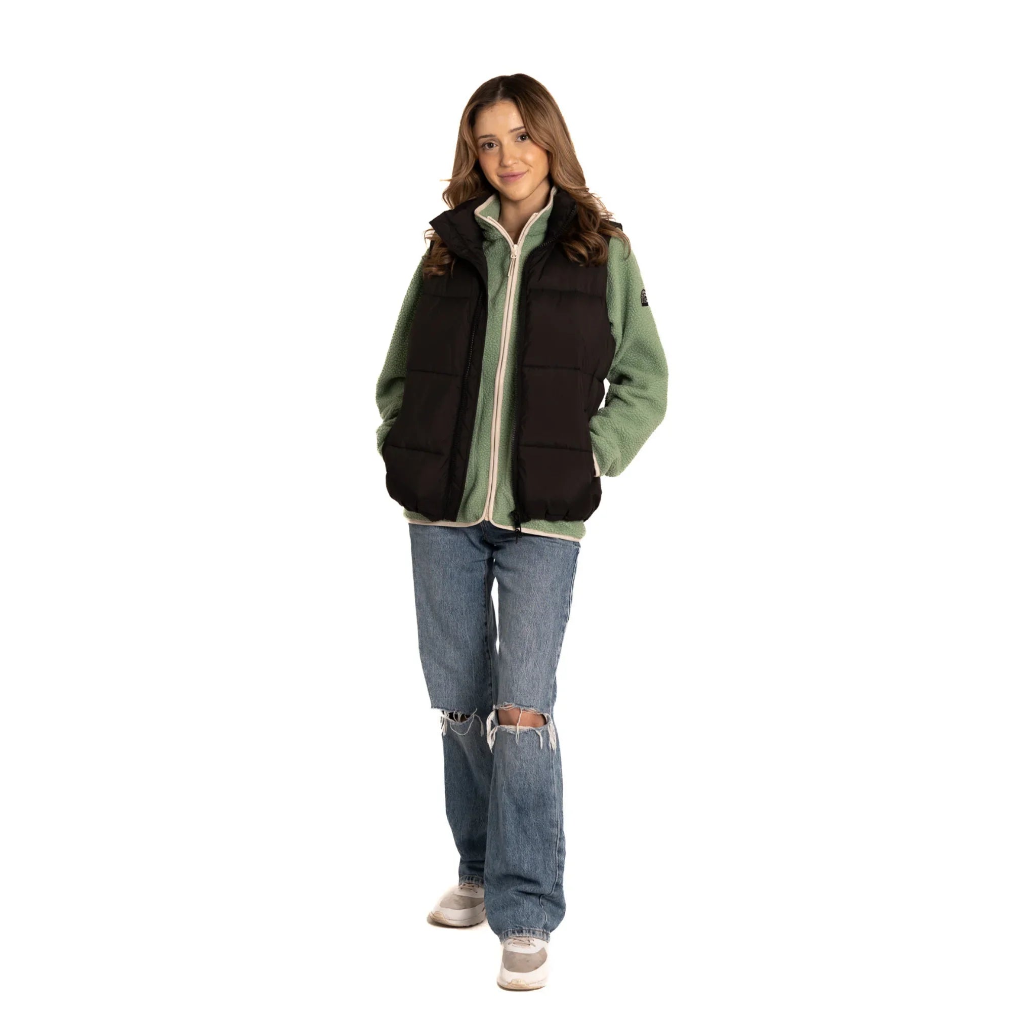 Woman wearing black puffer vest, green fleece jacket, ripped jeans, and sneakers