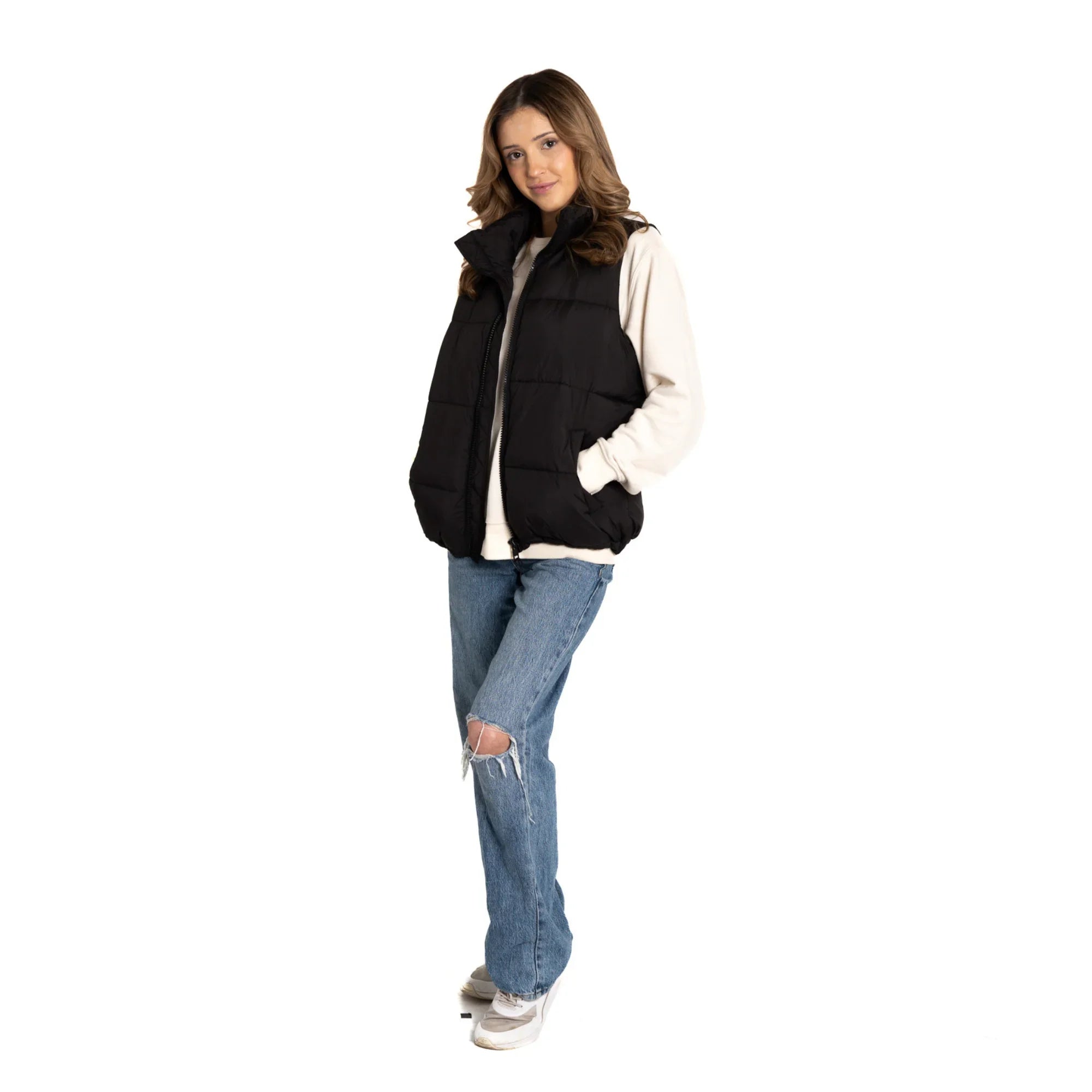 Woman in black puffer vest, white sweatshirt, ripped blue jeans, and sneakers