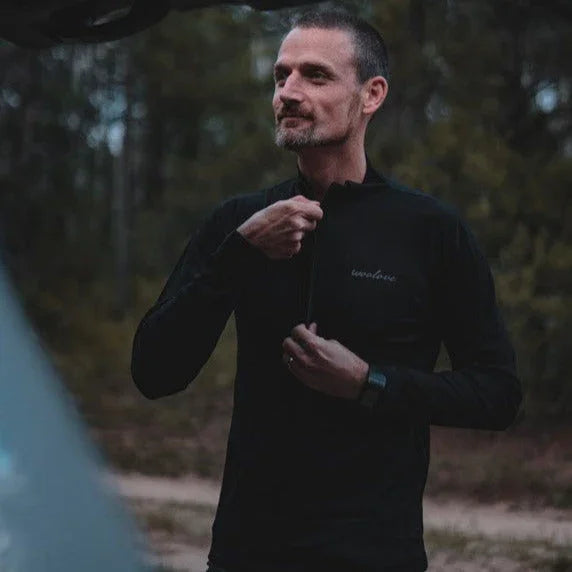 Man wearing black quarter zip pullover outdoors in a forest setting