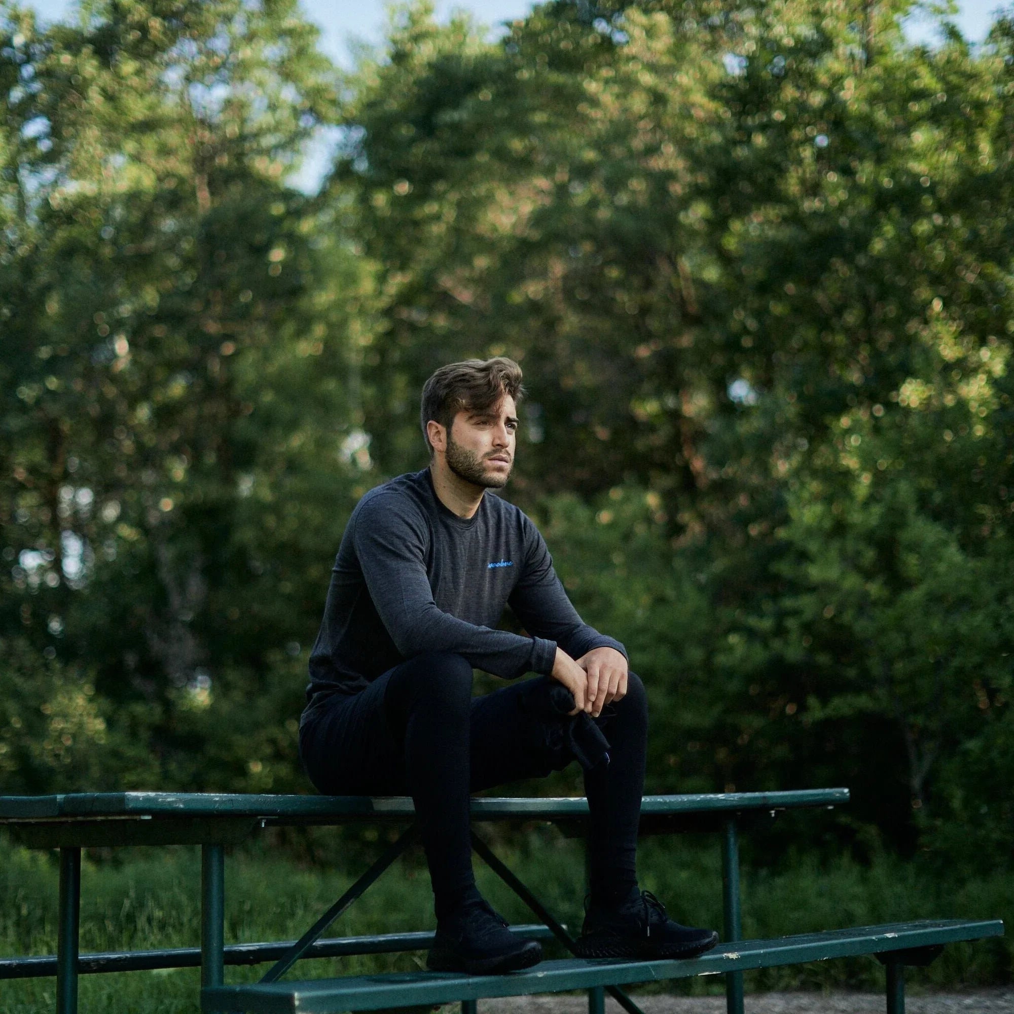 Man in dark merino wool long sleeve shirt sitting on green bench outdoors in nature