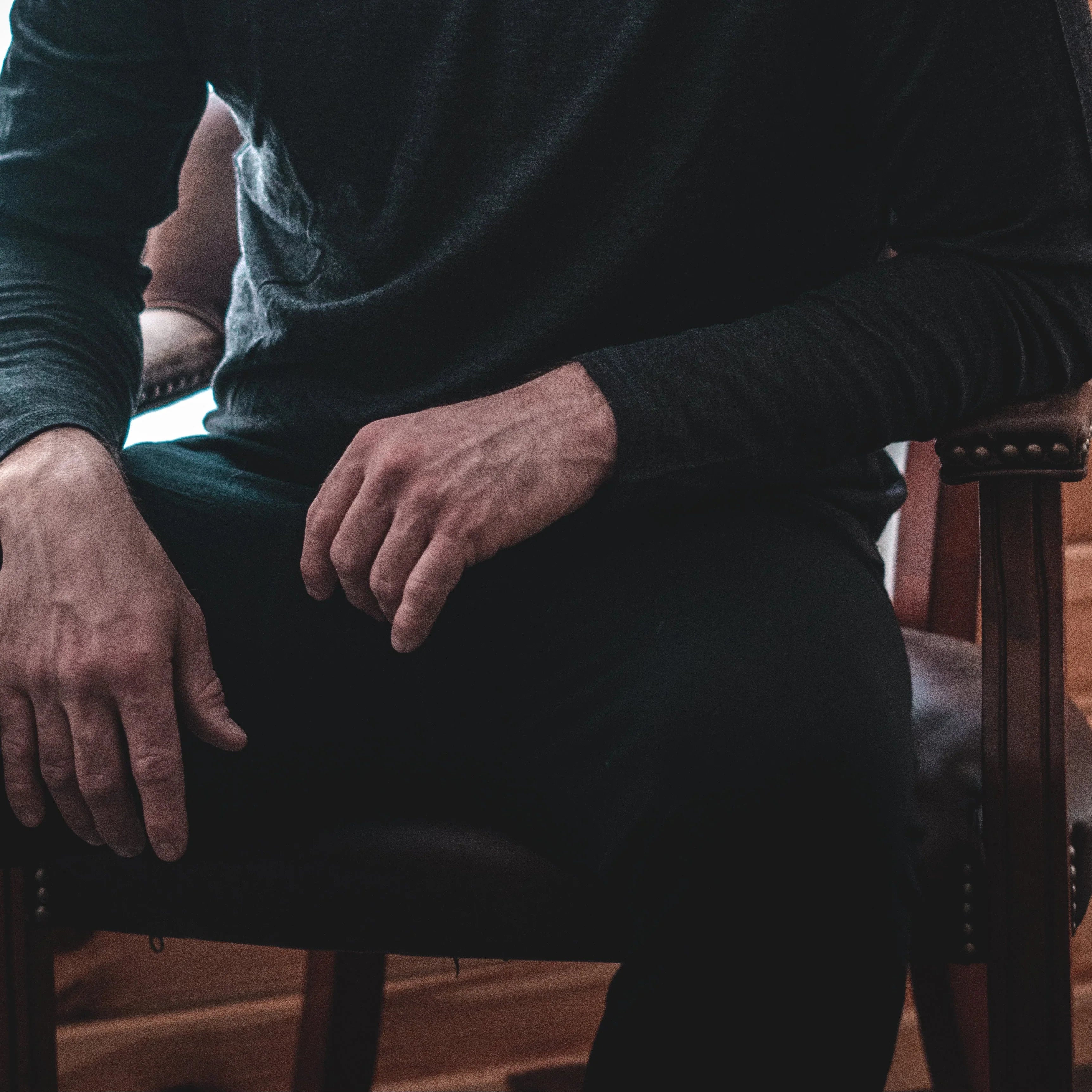 Man in dark long sleeve shirt and black pants sitting on a brown leather chair