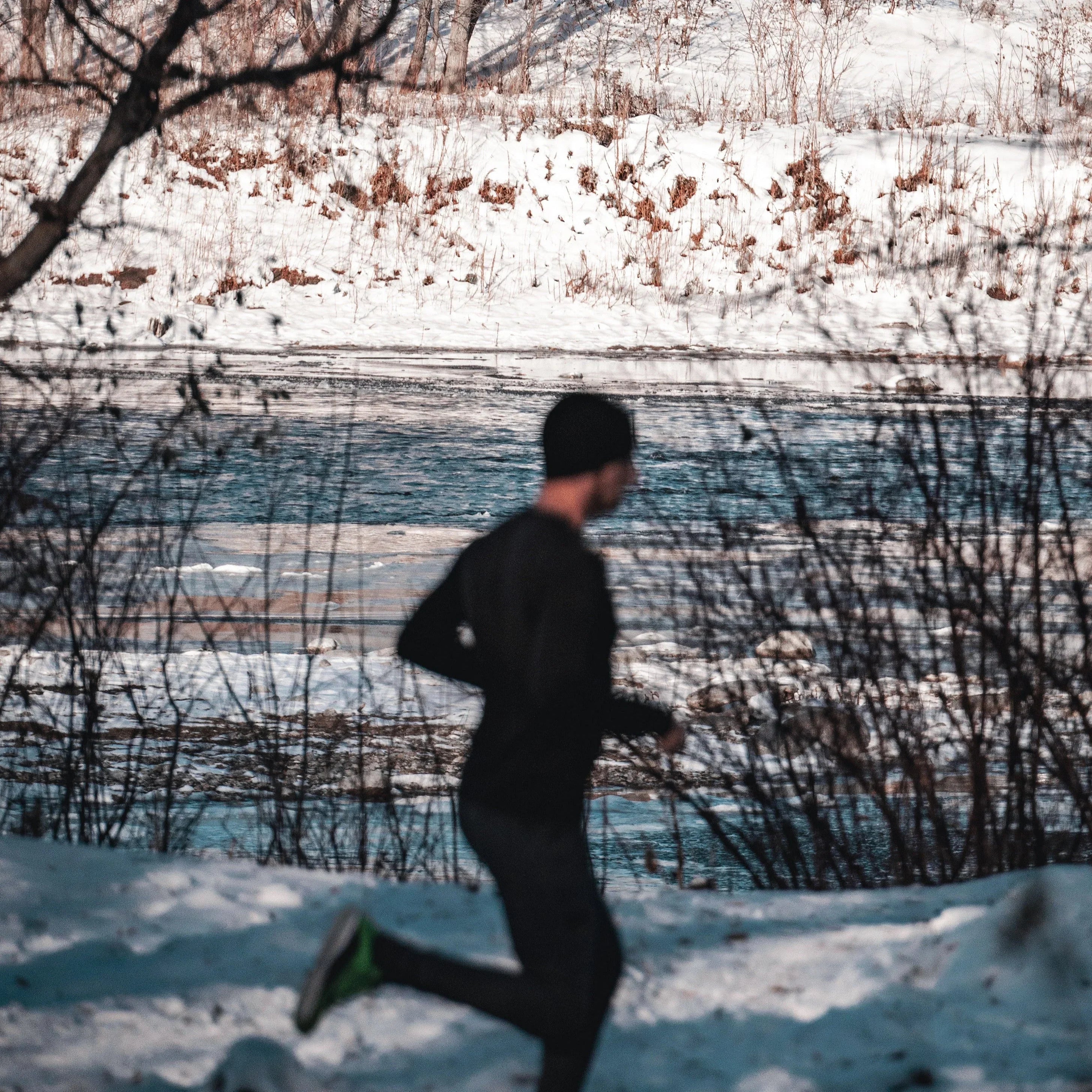 Man jogging in winter near a snowy riverbank, outdoor exercise in cold weather