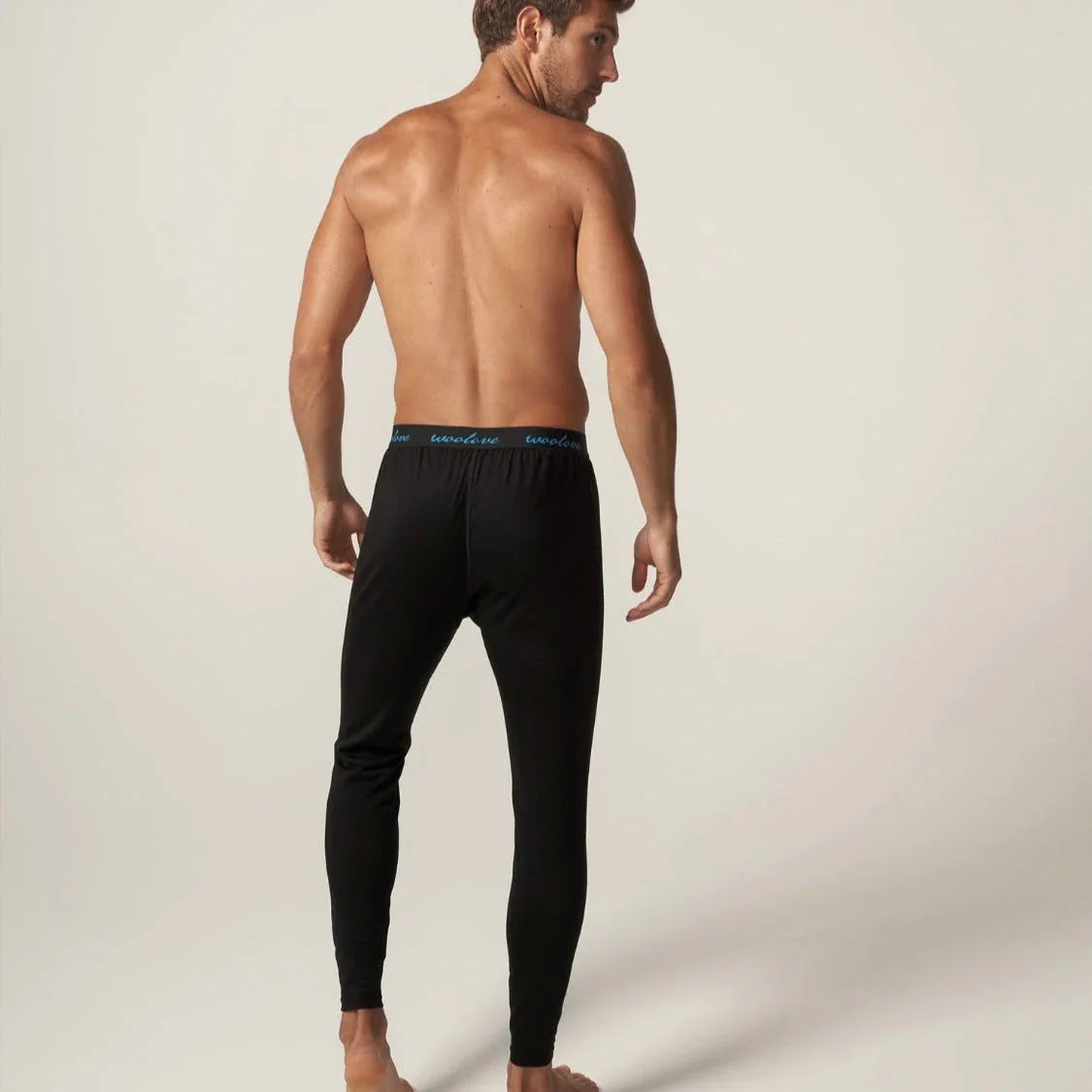 Man wearing black merino wool long underwear leggings, back view, plain background