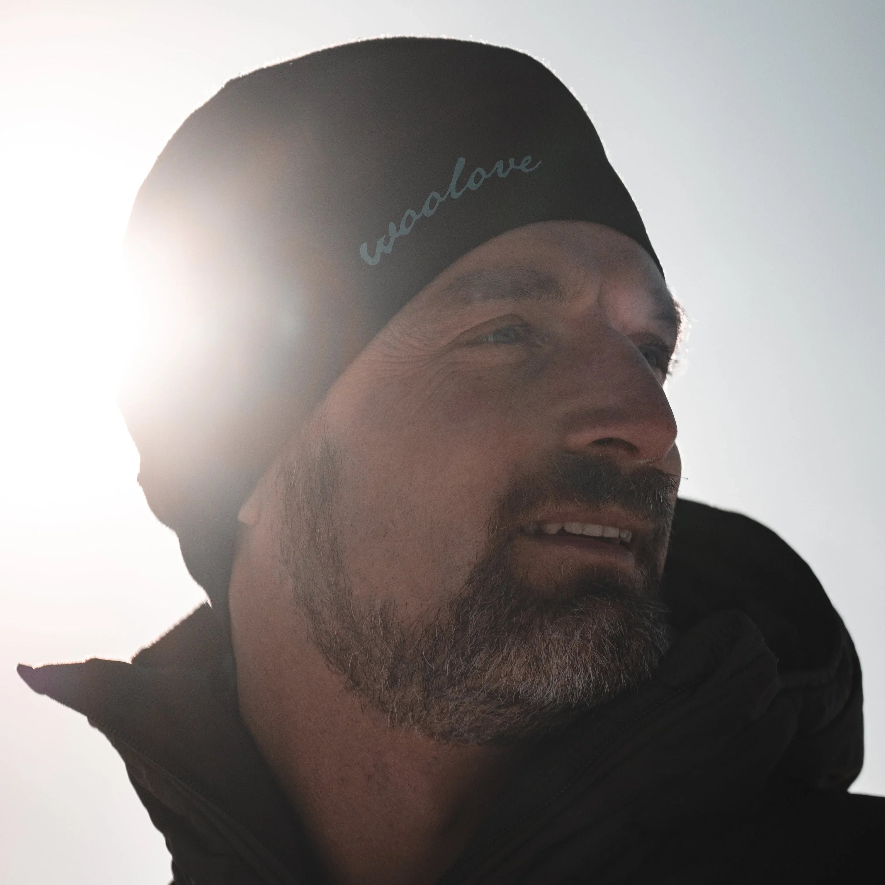 Man in black woollove beanie and jacket outdoors in bright sunlight