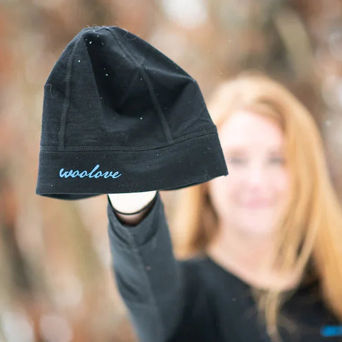 Woman holding up a black Woolove beanie outdoors in winter