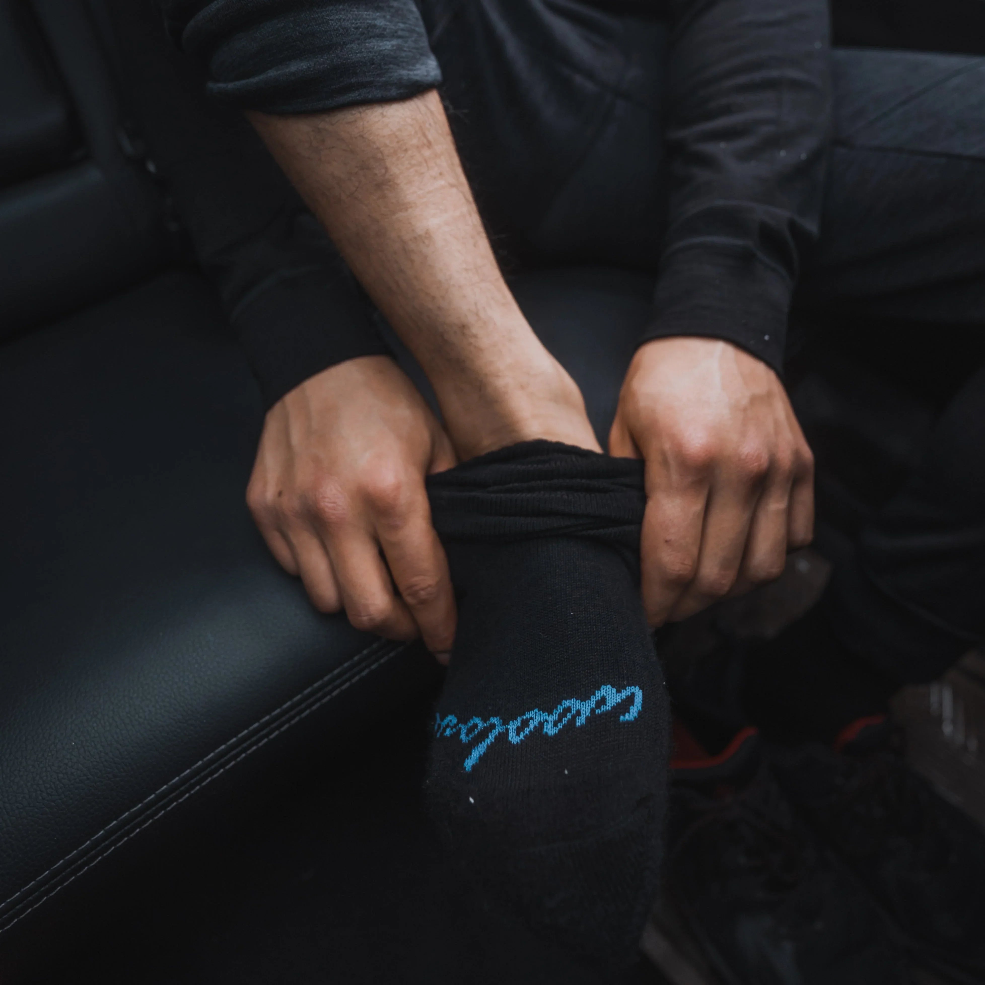 Person putting on black mountain socks in car interior, close-up of hands and sock detail