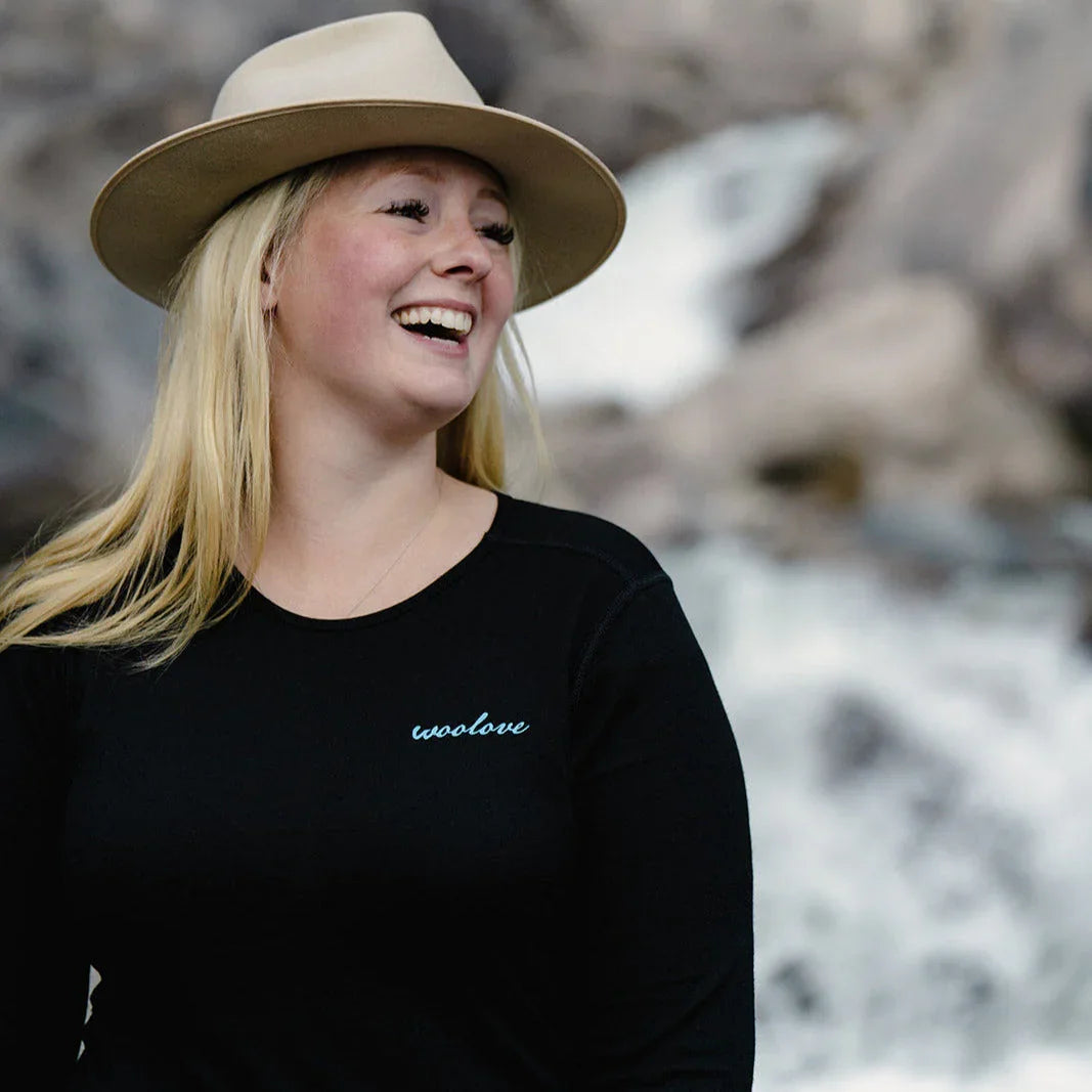 Smiling woman in a beige hat and woolove black shirt outdoors by a waterfall