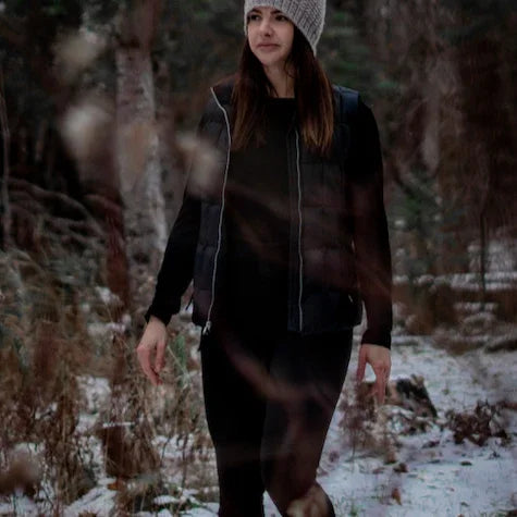 Woman wearing black leggings and vest walking in snowy forest, winter outdoor fashion