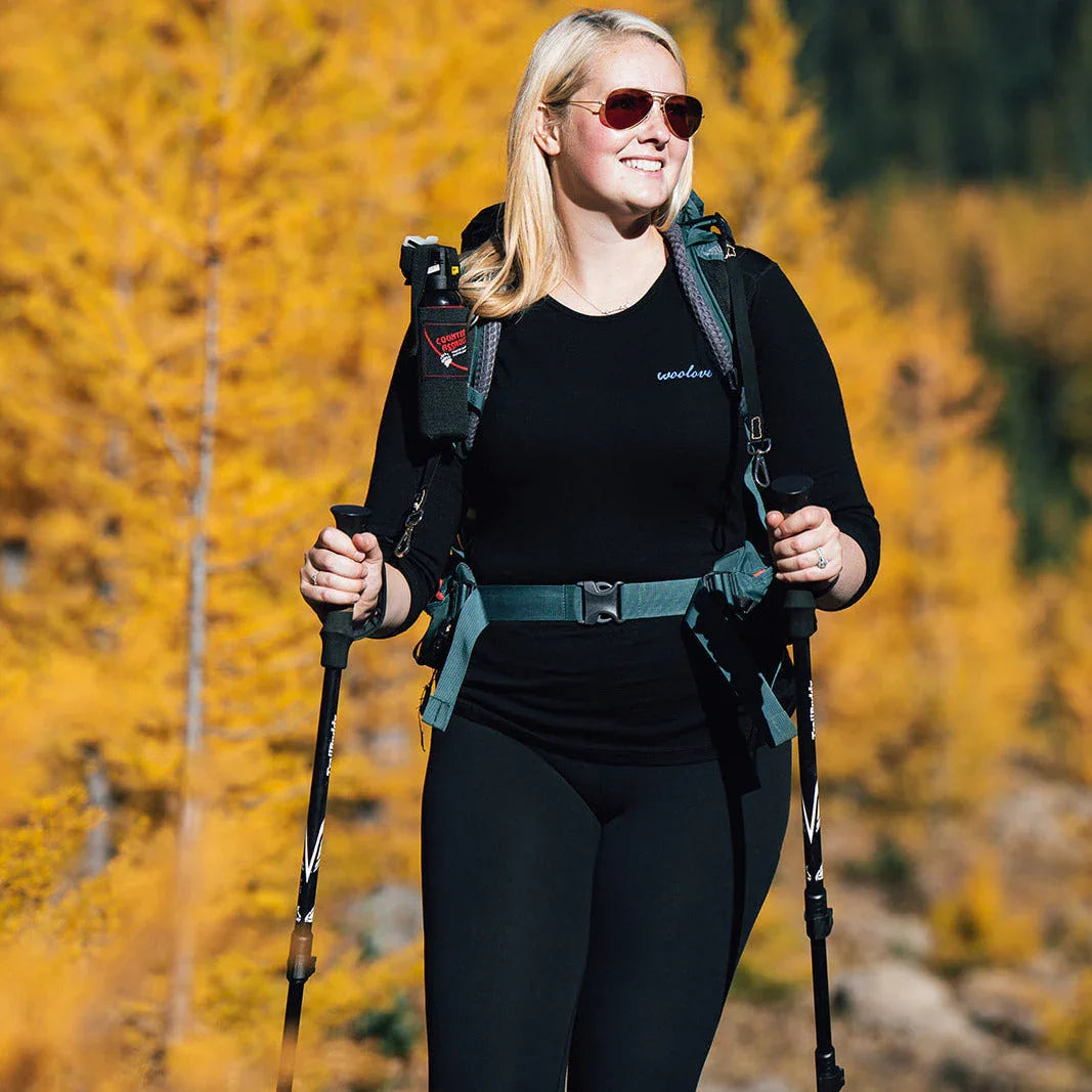 Woman hiking in autumn forest wearing black Woolove shirt, backpack, and sunglasses