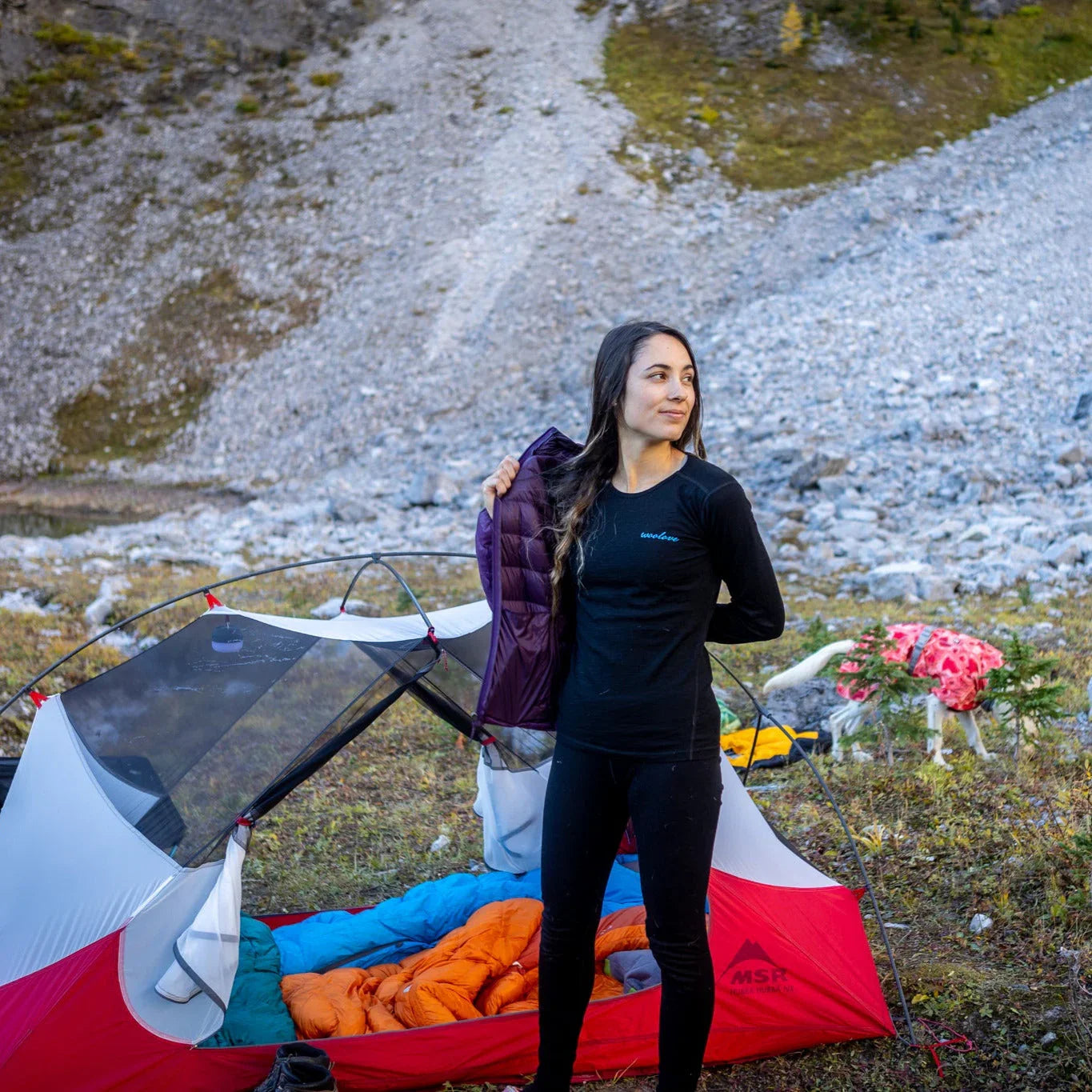 Woman in black Woolove shirt at campsite by tent and sleeping bags in rocky mountain setting