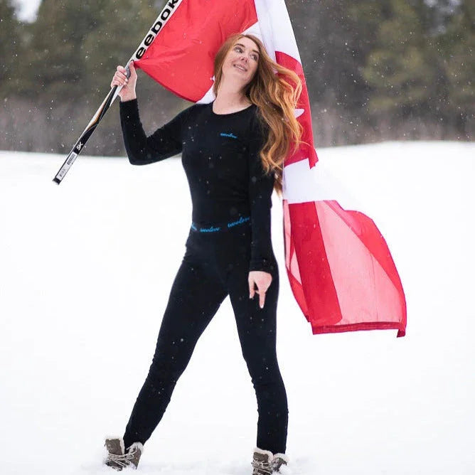 Woman in black thermal wear holding hockey stick and Canadian flag in snowy outdoors