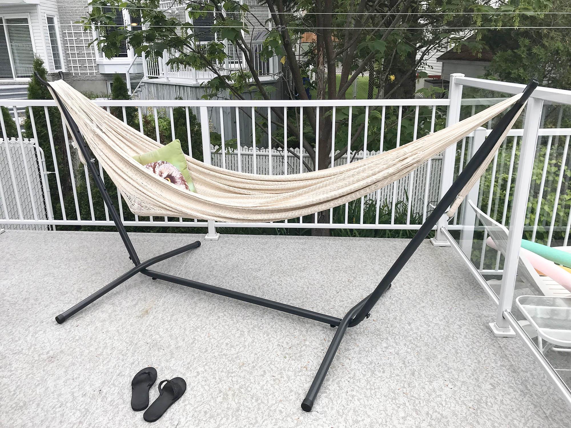 Natural Mayan hammock with black universal stand on outdoor patio, green pillow, black sandals