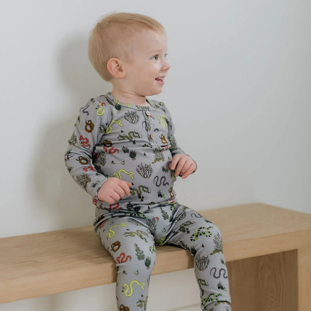 Toddler wearing grey snake print pajamas sitting on a wooden bench indoors