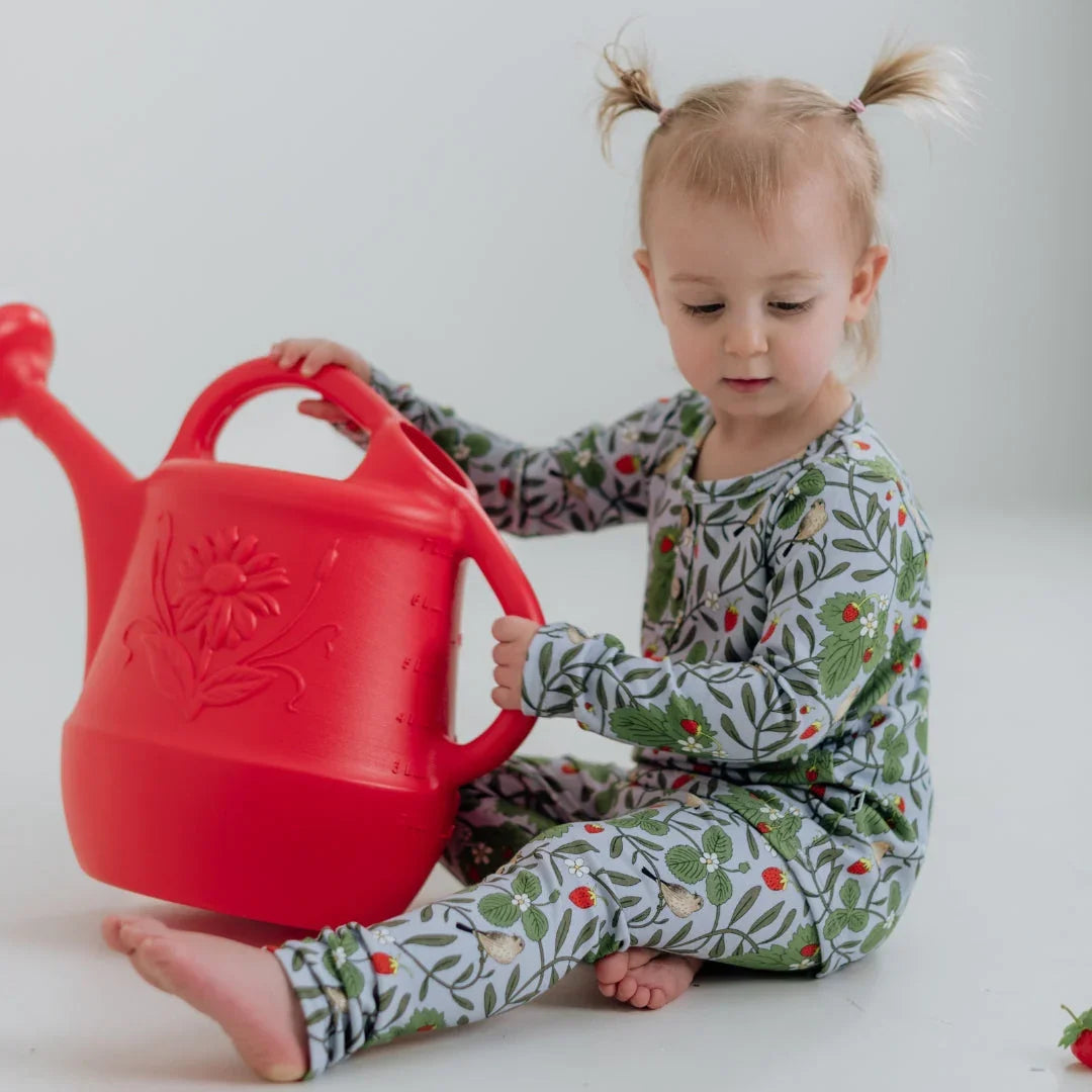 Toddler in floral pajamas holding large red watering can on white background