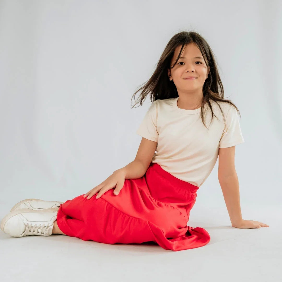 Girl in white t-shirt and red skirt sitting on white studio background, casual kids fashion