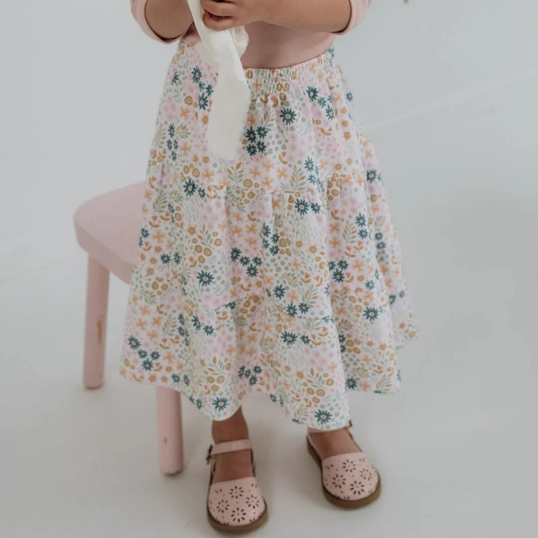 Child wearing floral bamboo Aria skirt and pink shoes in a bright room