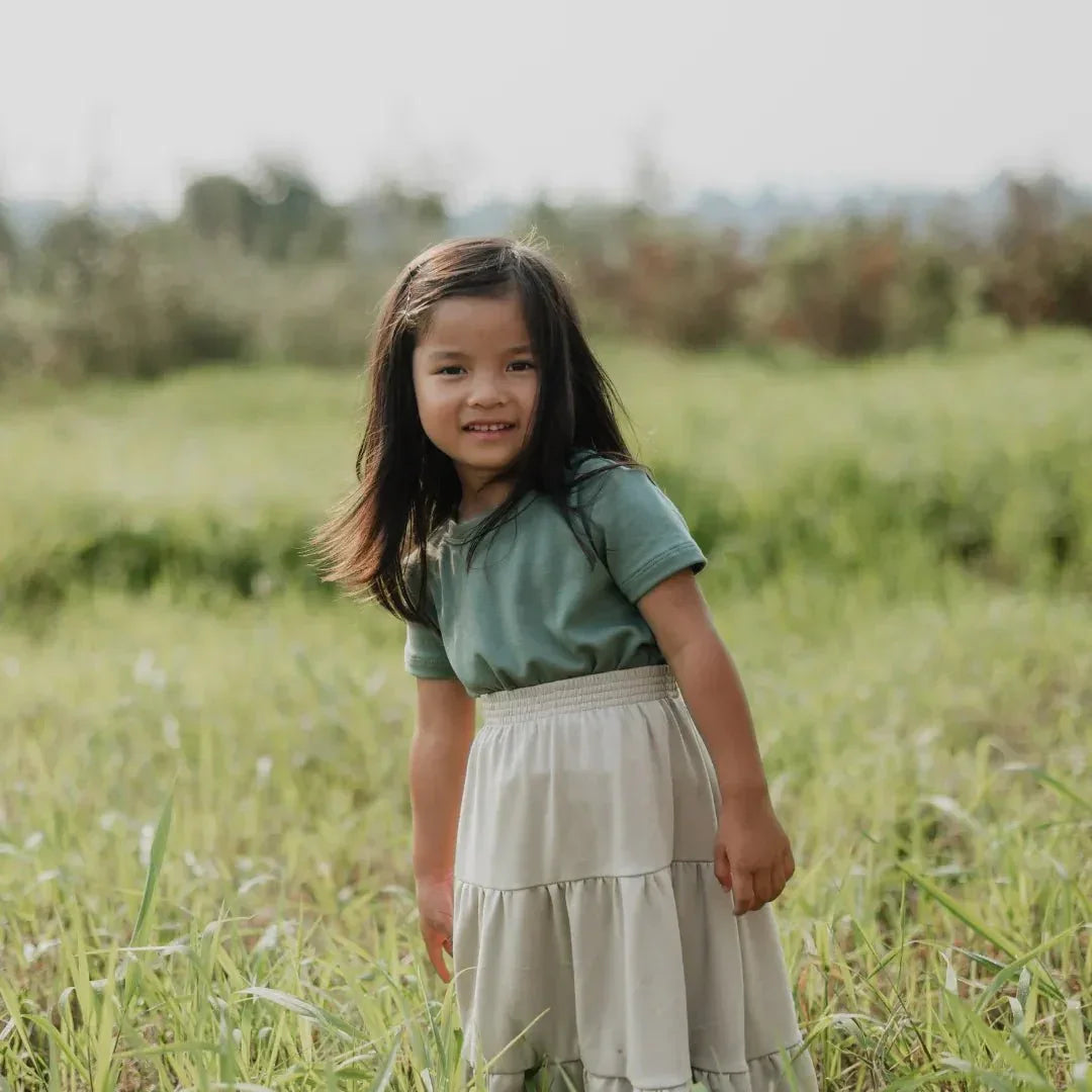 Girl wearing green top and bamboo Aria skirt standing in grassy field outdoors