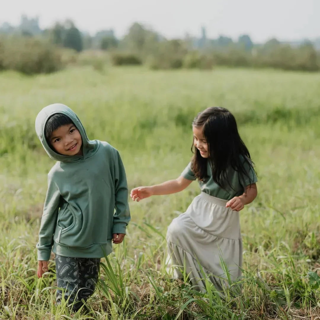 Two children in green bamboo Aria skirt outfits playing in a grassy field
