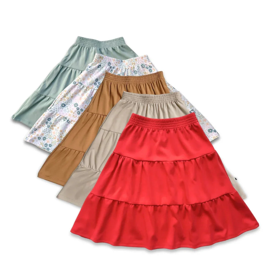 Assorted kids tiered skirts in red, tan, beige, mint green, and floral print, laid flat