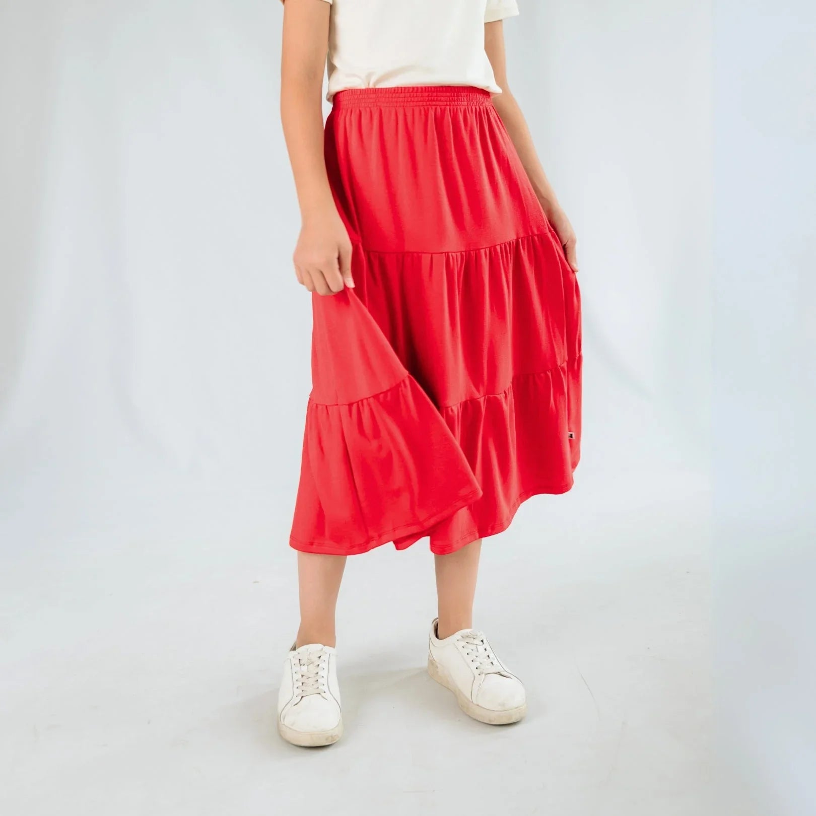 Girl wearing a red tiered midi skirt, white t-shirt, and white sneakers in studio